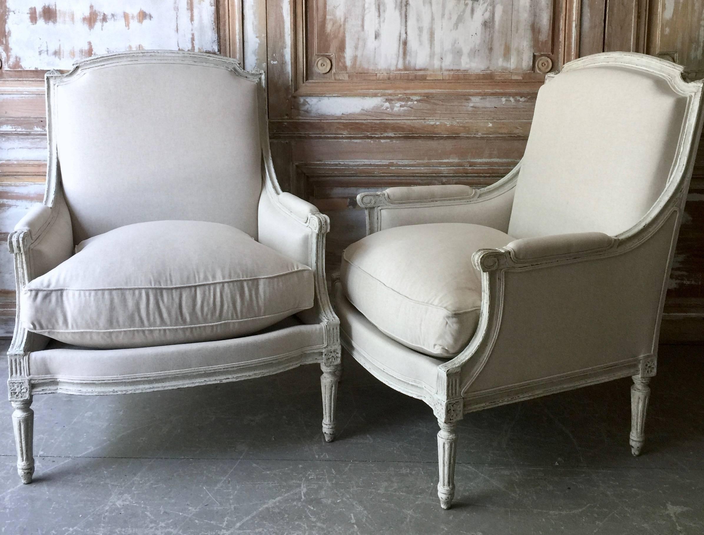 A pair of French painted Bergères in Louis XVI taste, with generous seats and flat backs are "en chapeau" ( arched with the arch-springs indented ) The wood frames are in lovely gray painted finish with richly carved frame, fluted leg and