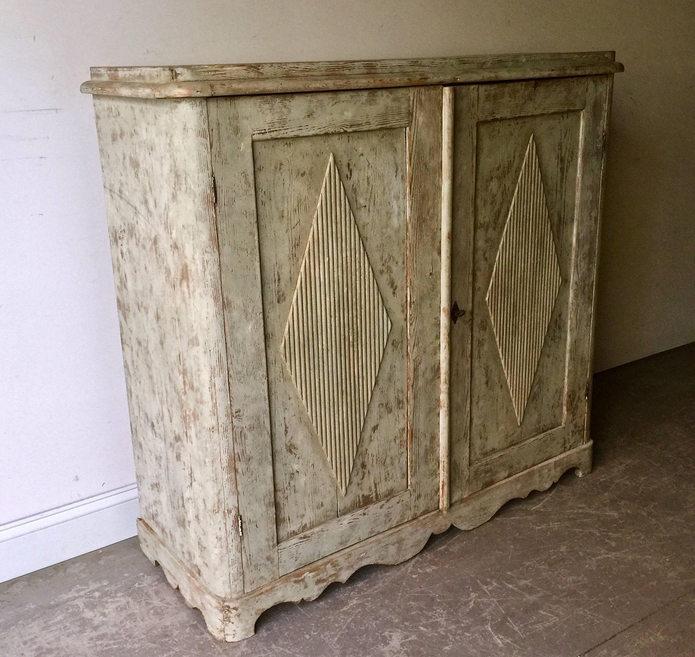19th century Swedish Gustavian sideboard with classic Gustavian motifs; diamond shaped panelled doors on beautifully scallop-shaped apron. Inside with two shelves and two drawers. Scraped back to remnants of its original cream/greenish/ paint.