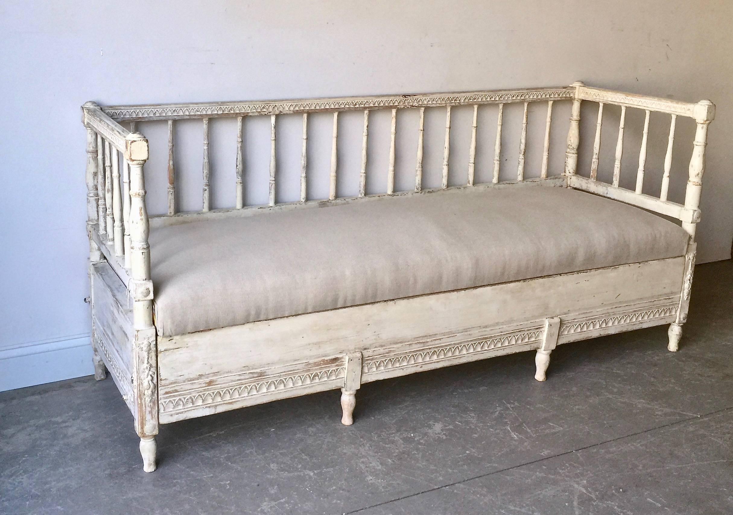 Gustavian sofa bed, Sweden circa 1850 with beautiful Gustavian details; the back rail and apron with standing stylized leaf carvings and the carving on the columns. The finish has been scraped to reveal much of the original cream/white paint. Seat