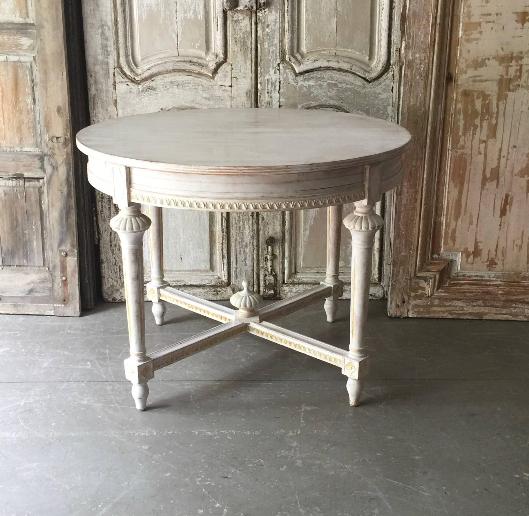 Swedish Gustavian style round table with richly carved apron, tapering carved legs and saltire strecher with central medallion in painted worn cream patina, Sweden, circa 1880.