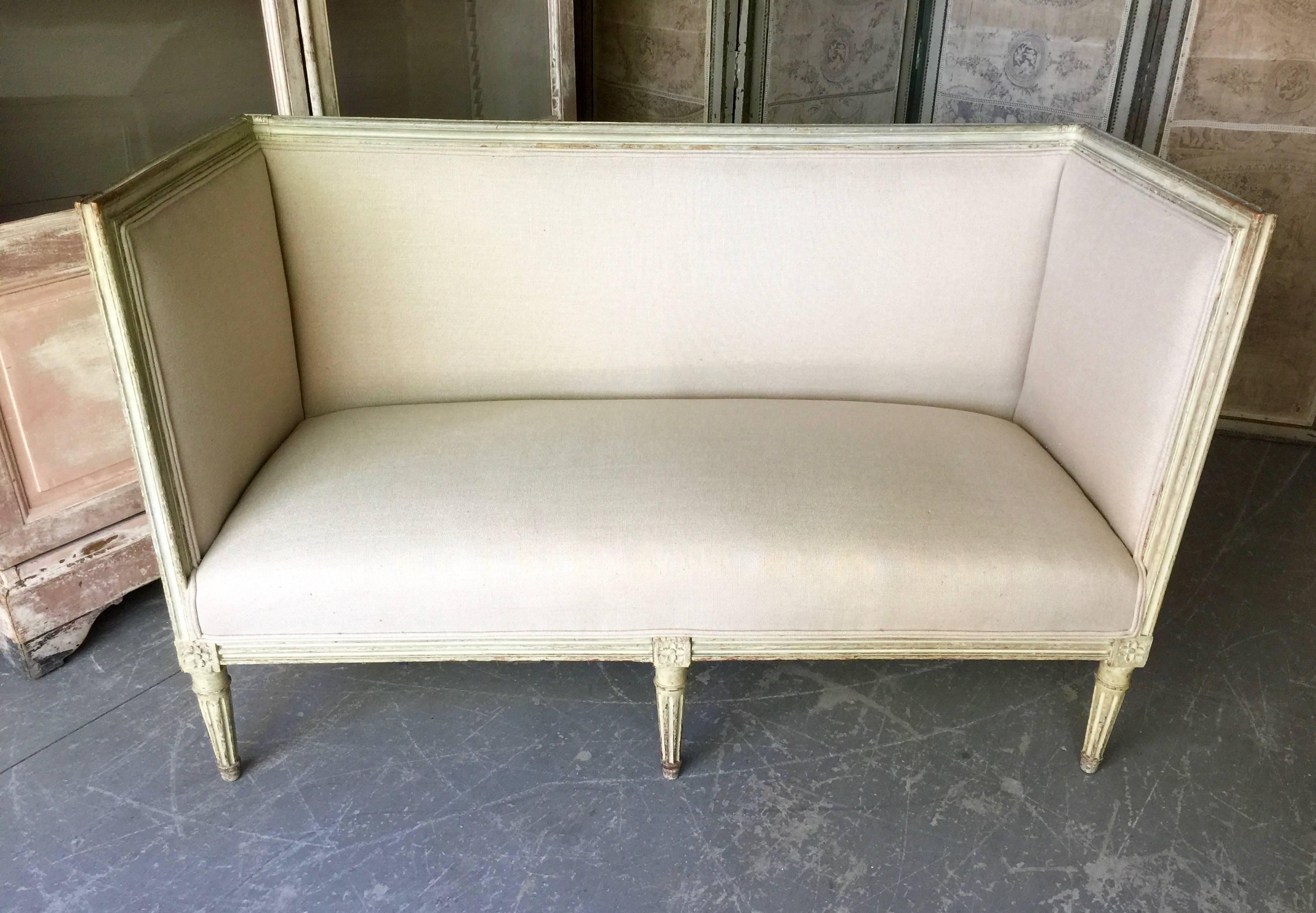 19th century French Louis XVI style painted settee in rectangular form. 
The wood frames are in lovely cream/greenish painted finish with richly carved frame, fluted leg and cubic blocks decorated with florets. Completely re-upholstered in