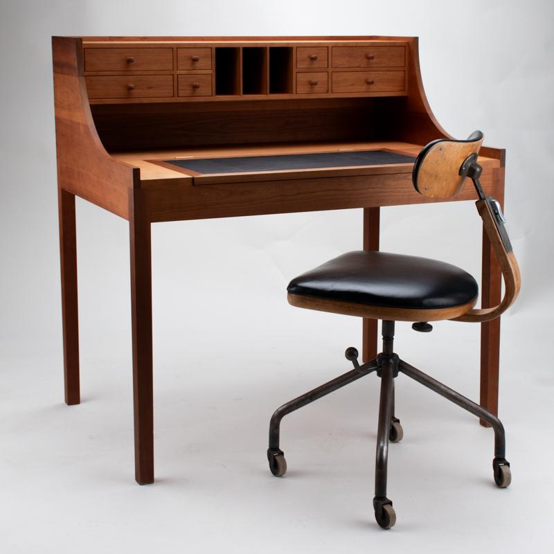 Uno scrittoio raffinato e funzionale dell'ebanista danese Per Hermansen, realizzato in solido legno di ciliegio americano. La scrivania è dotata di otto piccoli cassetti e di una superficie di scrittura ribaltabile intarsiata in pelle nera, che