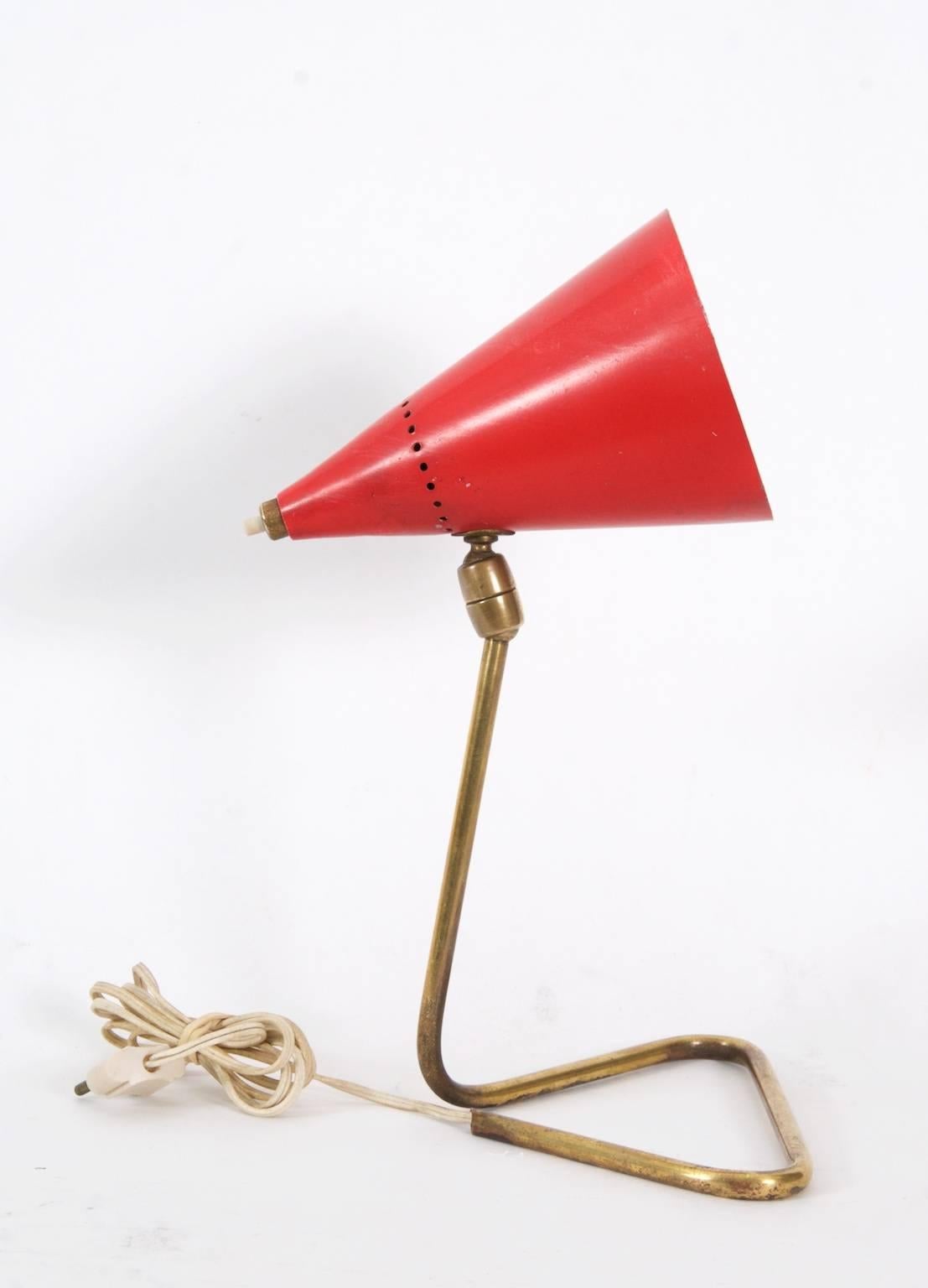Italian table lamp attributed to Stilnovo, Italy, circa 1950.
Enamelled red cone shade with press button switch mounted on a brass tubular base connected by a double ball joint. Original wiring present, in working condition, should be rewired if