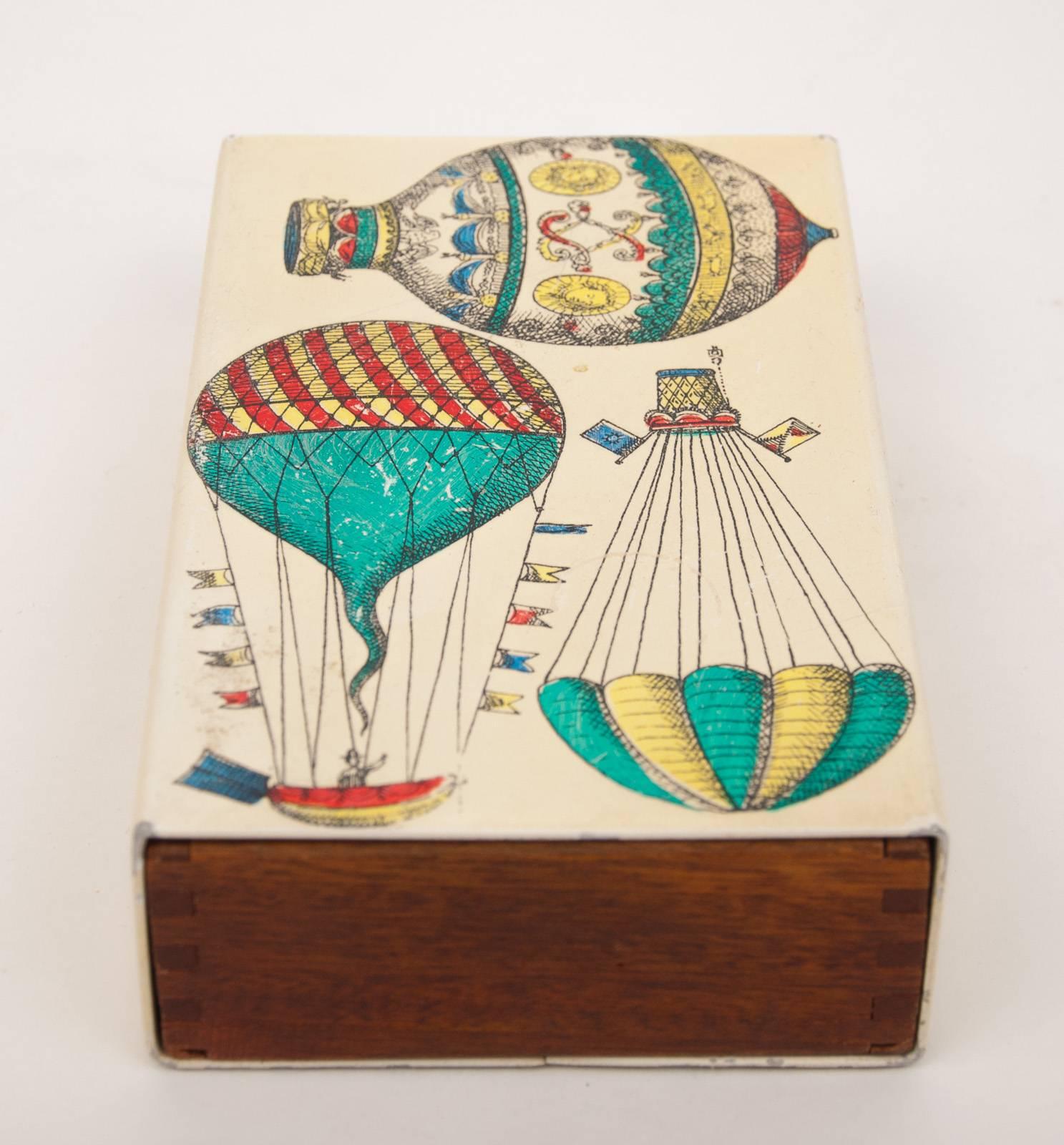 A Piero Fornasetti box decorated with hot air balloons.
Metal, lithographically printed and hand colored.
Mahogany interior,
Italy, circa 1960.