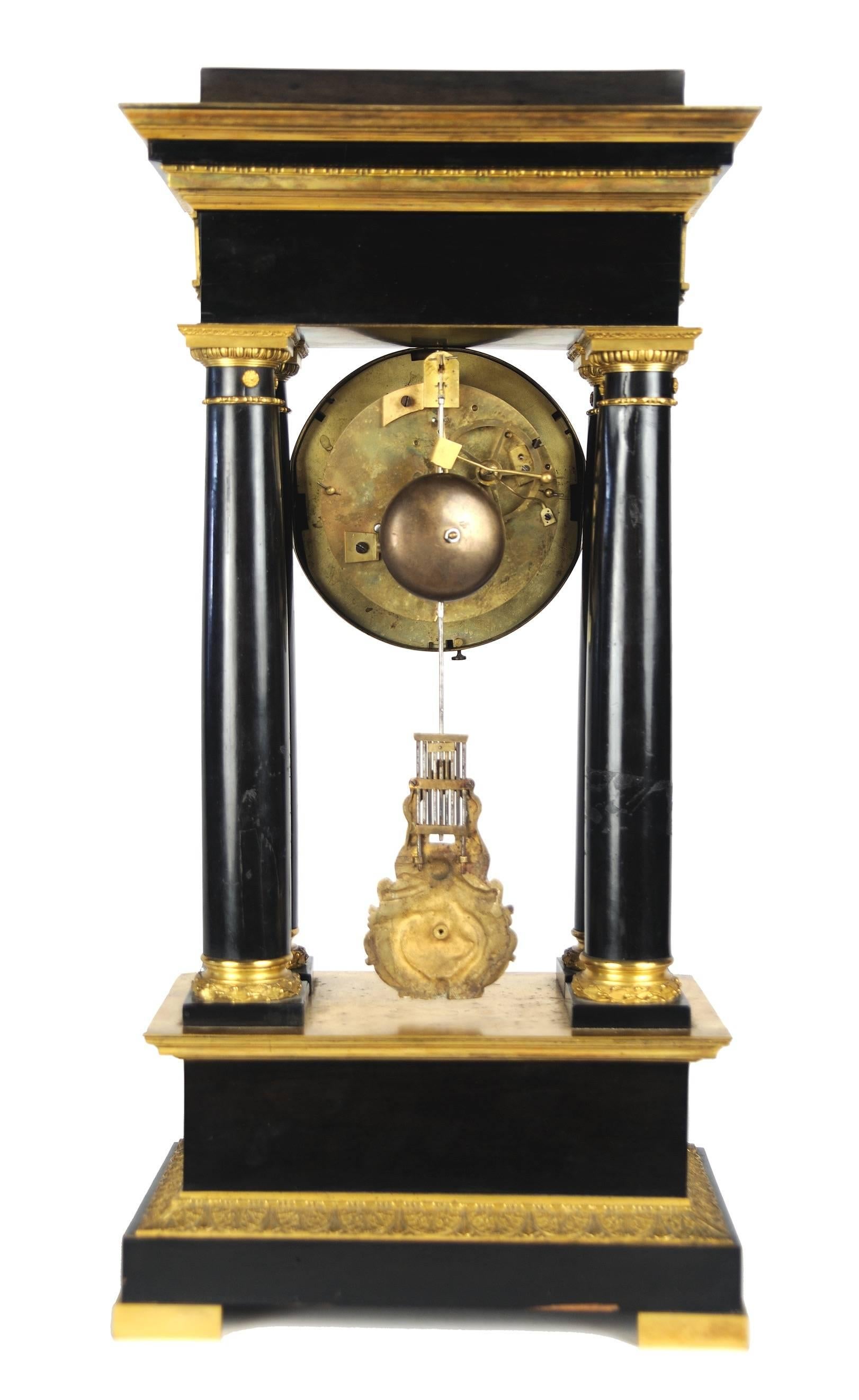 Gilt and ebony portico clock with magnificent ormolu clock face, frieze, column mounts and base. Clock is in working order and includes winding key. Accuracy is not guaranteed.