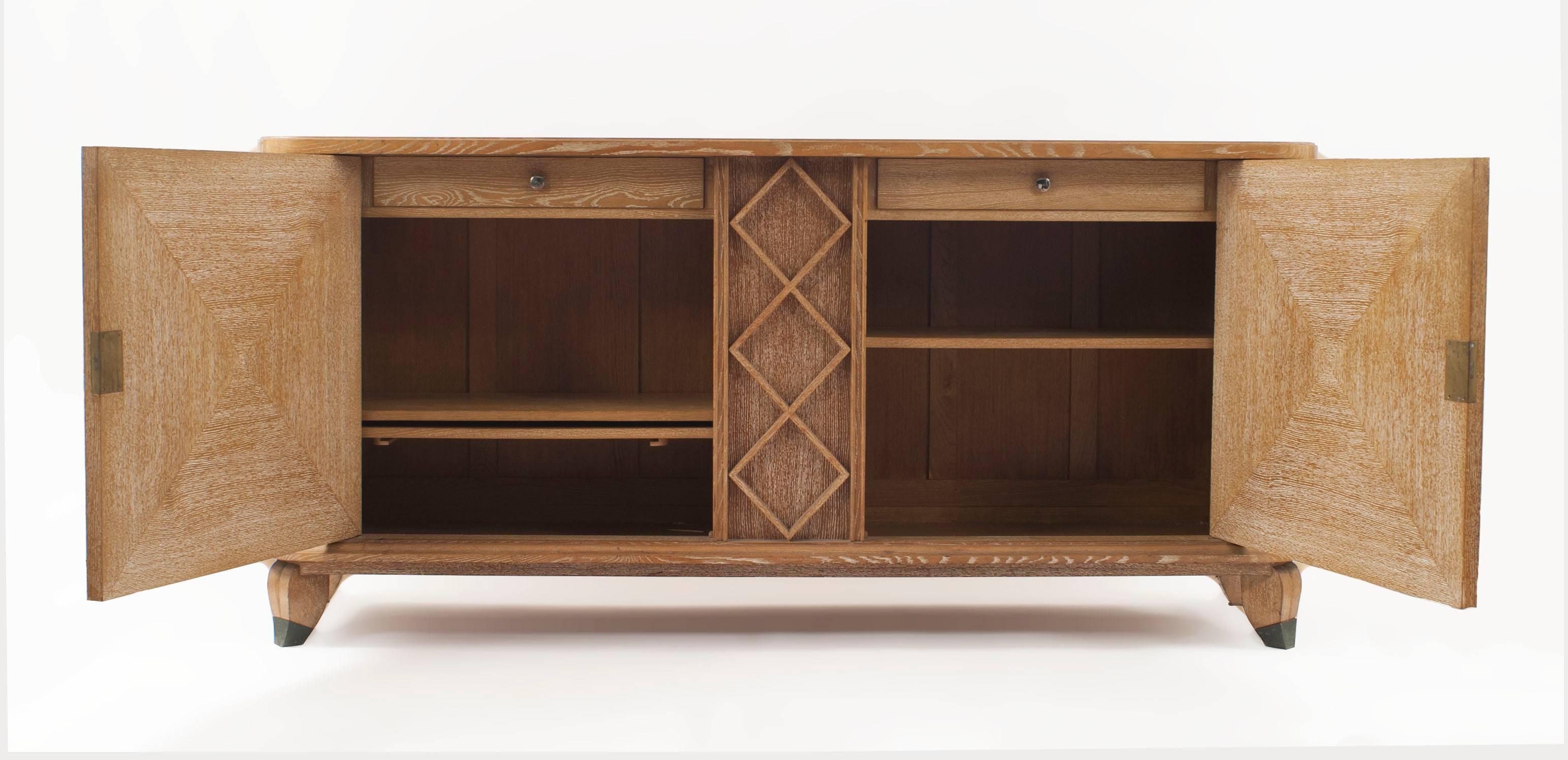 French mid-century (1940s) cerused oak buffet with two drawers behind two doors having centered ebonized bronze masks and trim with a geometric design centre panel (Andre Arbus).

André Arbus was a French furniture designer, sculptor and