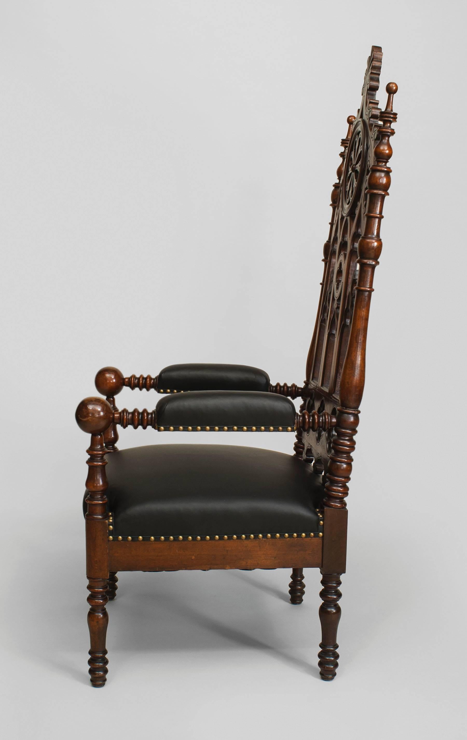 Pair of nineteenth century English Gothic Revival mahogany armchairs with brown leather seats and arm pads beneath high backs decorated with filigree carvings in imitation of Gothic architecture.
