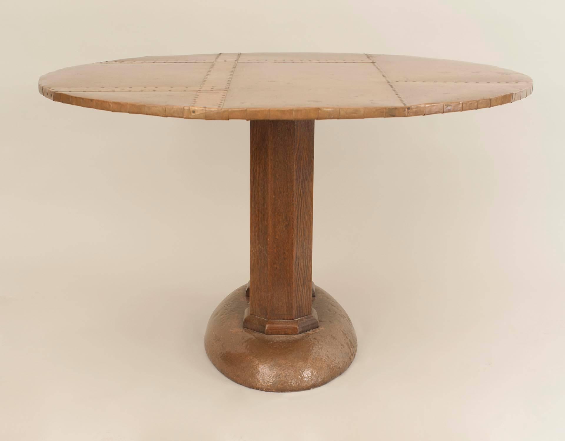 English Arts and Crafts center table with a round copper sheathed top supported by a pair of oak column pedestals over an oval copper sheathed base.