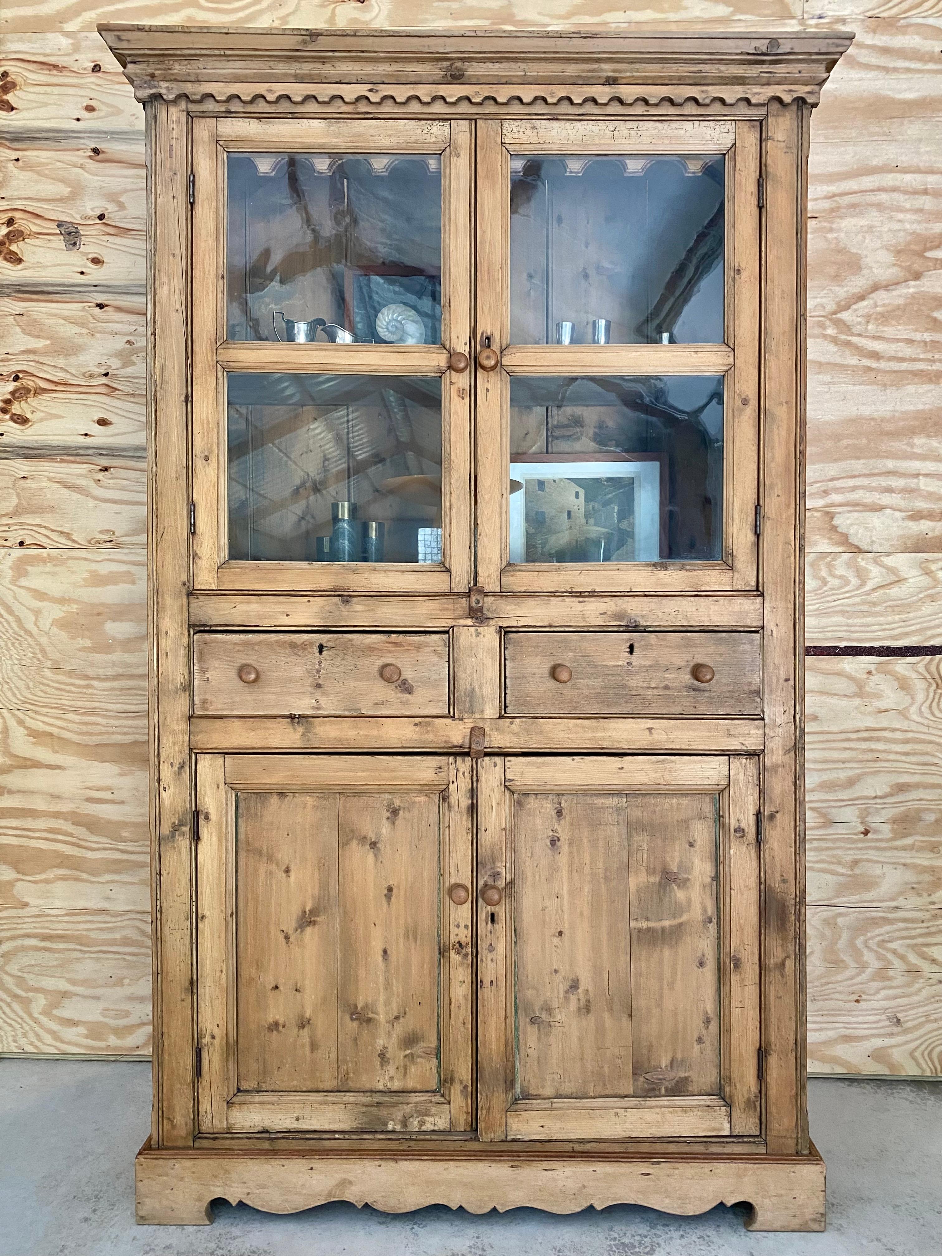 Il mobile in legno di pino, con ante ondulate in vetro sopra e un contenitore nascosto sotto, combina magnificamente il fascino rustico con i dettagli architettonici tradizionali. Il mobile superiore è dotato di due ante con pannelli in vetro dalle