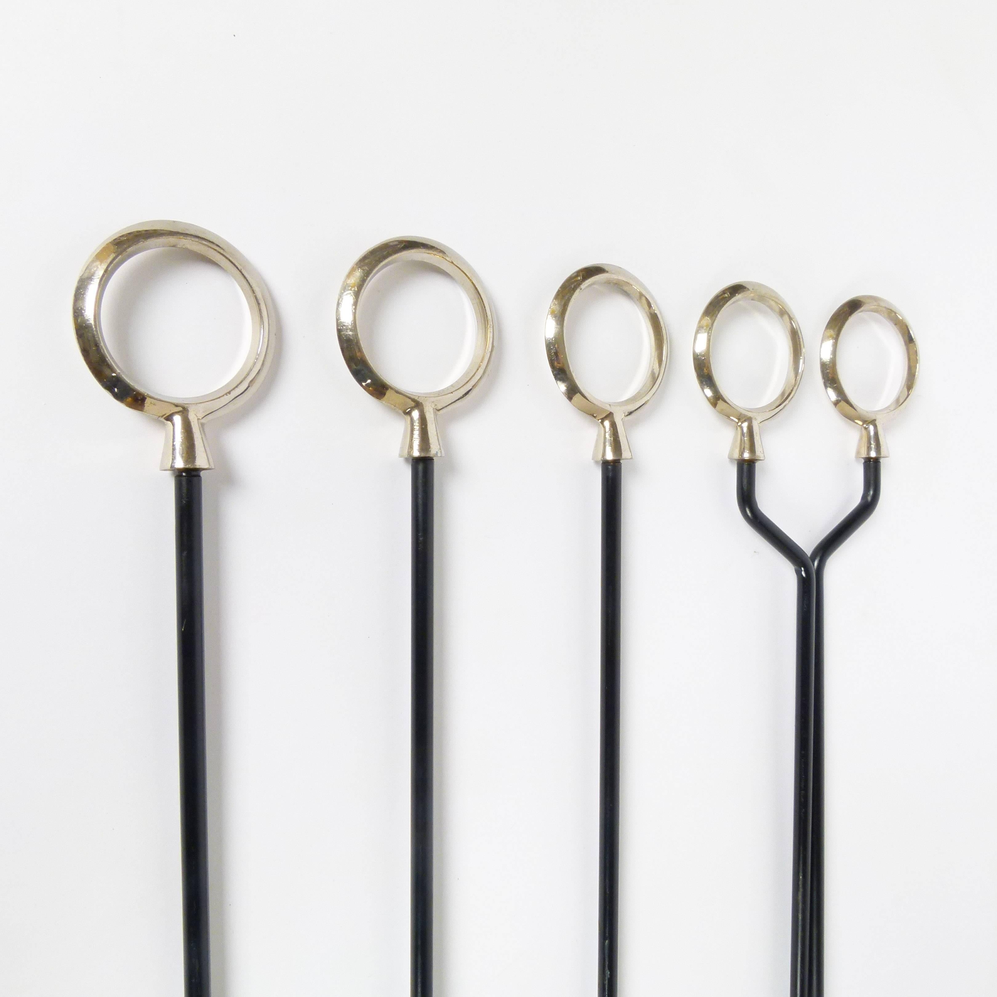 Refined Mid-Century Modern, circa 1960, fireplace tool set in wrought iron with black enamel coating, nickel plate handles, and period-correct wall-mounted hangers. Unusual extended length. Set includes four tools and two iron wall-mount hangers.