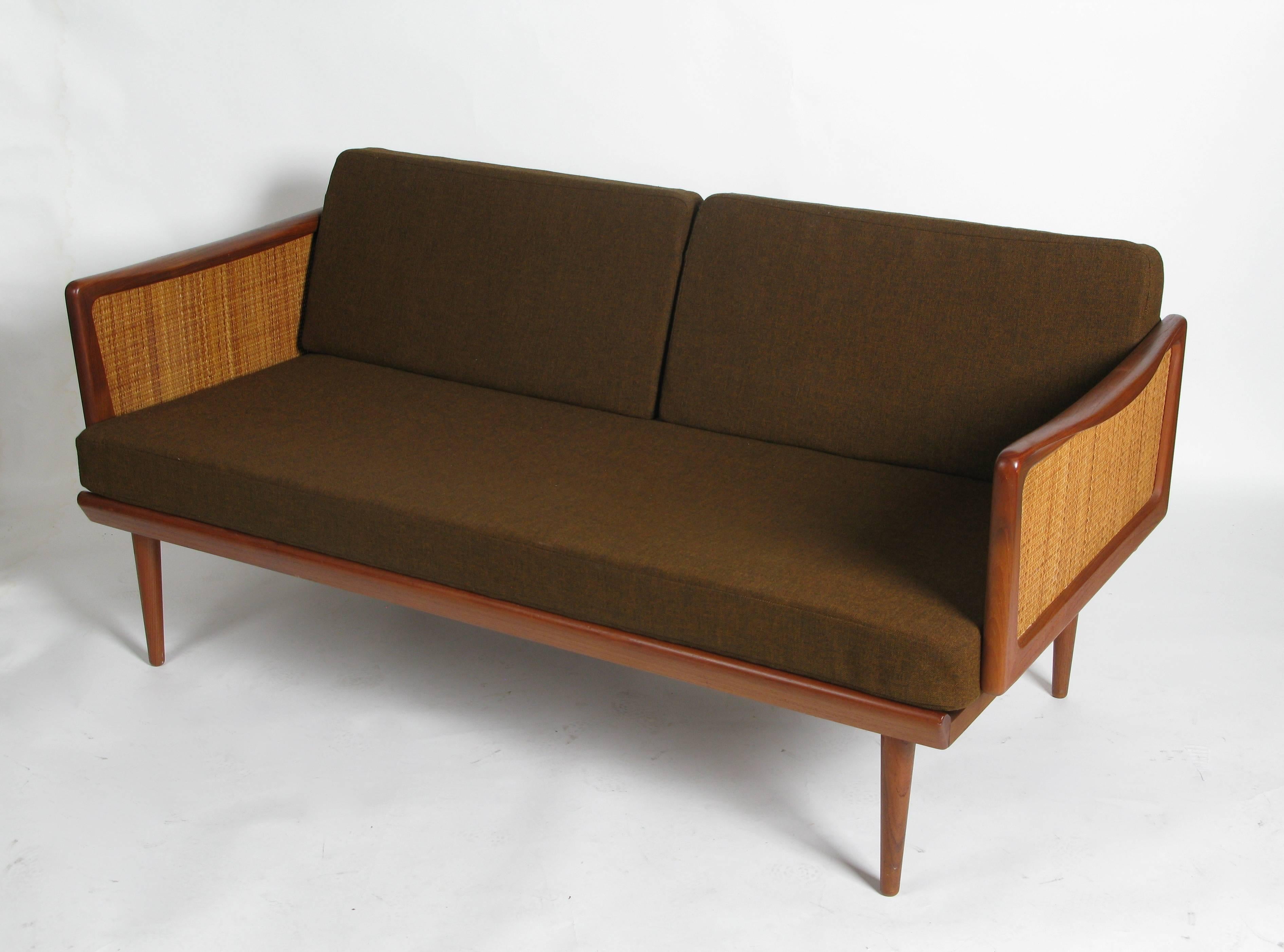 1960s model 453 daybed/sofa beautifully crafted of solid teak with modern cane arm detail by Peter Hvidt, Denmark.  Using solid brass hardware, the arms fold down extending the sofa to an extra long, single size bed.  All original and in excellent
