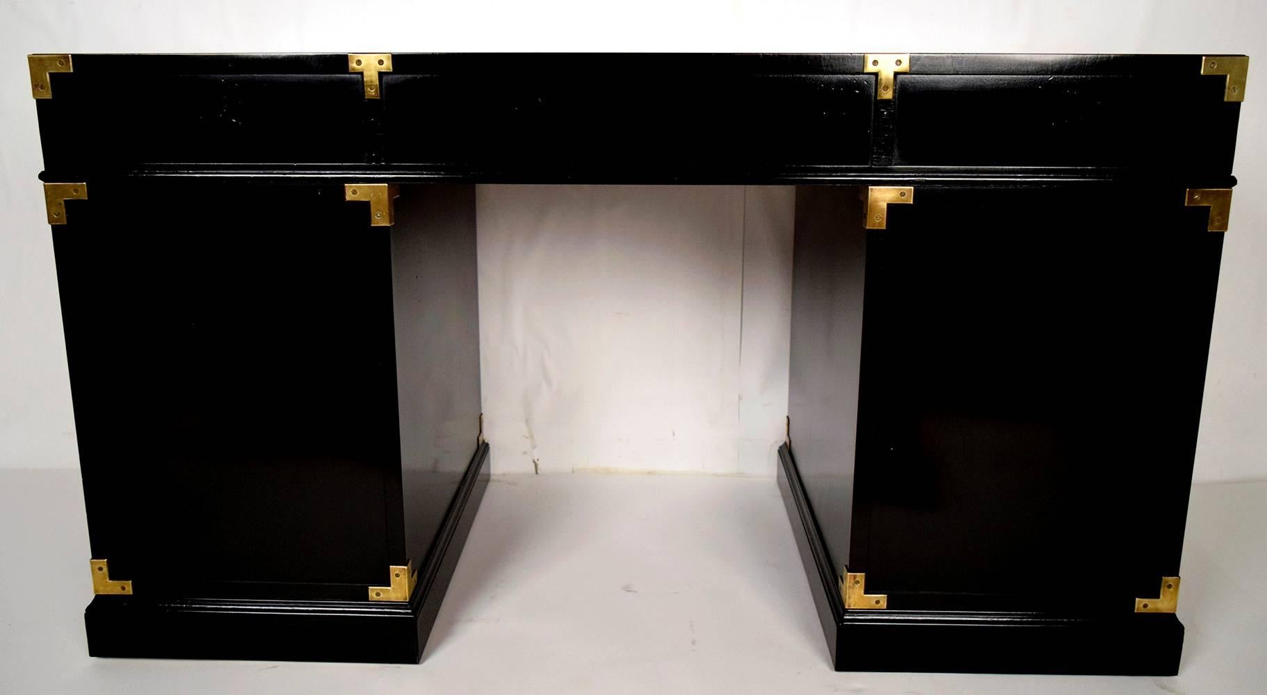 This is a 1970s desk by Henredon. Solid mahogany wood, newly finished in a rich black color in lacquered finish. Has brass decorations, with three drawers on top the side drawers have brass handles and the center has a design brass key-plate. The