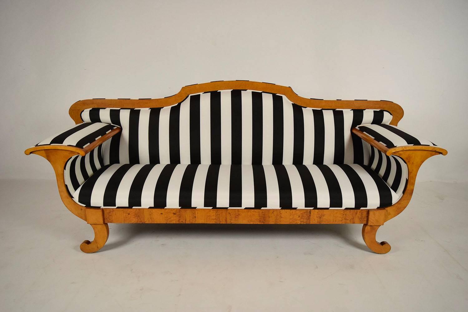This mid-19th century Biedermeier sofa is elegantly designed with a birch wood frame in its original golden color finish. The wood has a beautiful patina that compliments the new professional upholstery with a black and white striped fabric. The