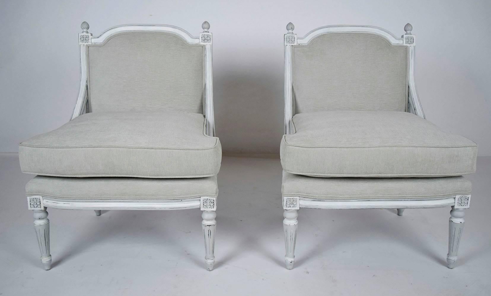 This pair of French Louis XVI-style bergeres features a walnut frame that has been painted in a grey and oyster color combination with a beautiful distressed finish. The frame is adorned with delicate carved moulding details with rosette details in