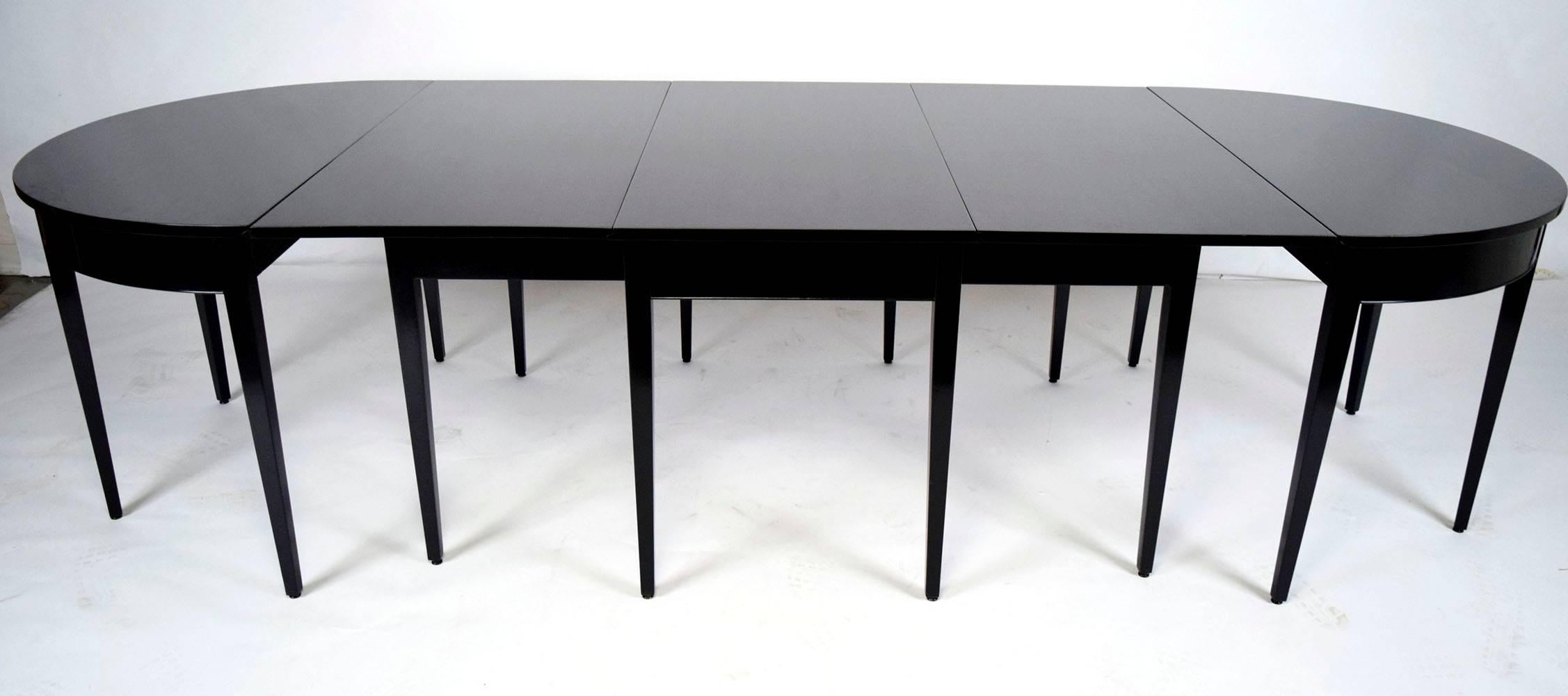 This 1930s, Federal-style hepplewhite dining table is made from mahogany wood that has recently been finished in a rich black color stain and a lacquered finish. The table separates into three parts. The center part is a rectangular table and there