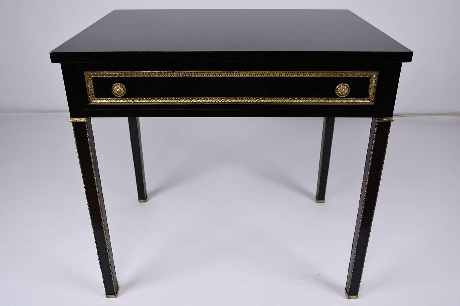 This 1910s antique French Louis XVI-style side table is made of mahogany wood that features a rich, ebonized finish. The single drawer is adorned with bronze moulding details and two decorative drawer pulls. The simple legs are accented by delicate