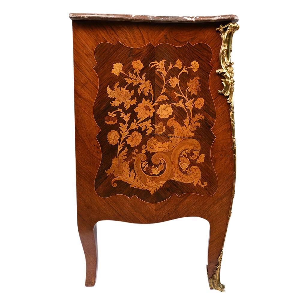 This 1880s Antique Louis XV-style chest of drawers or commode is made of wood that is adorned with beautiful marquetry details. The facades of the drawers and on the sides feature intricate inlaid wood designs of flowers and leaves inside a delicate