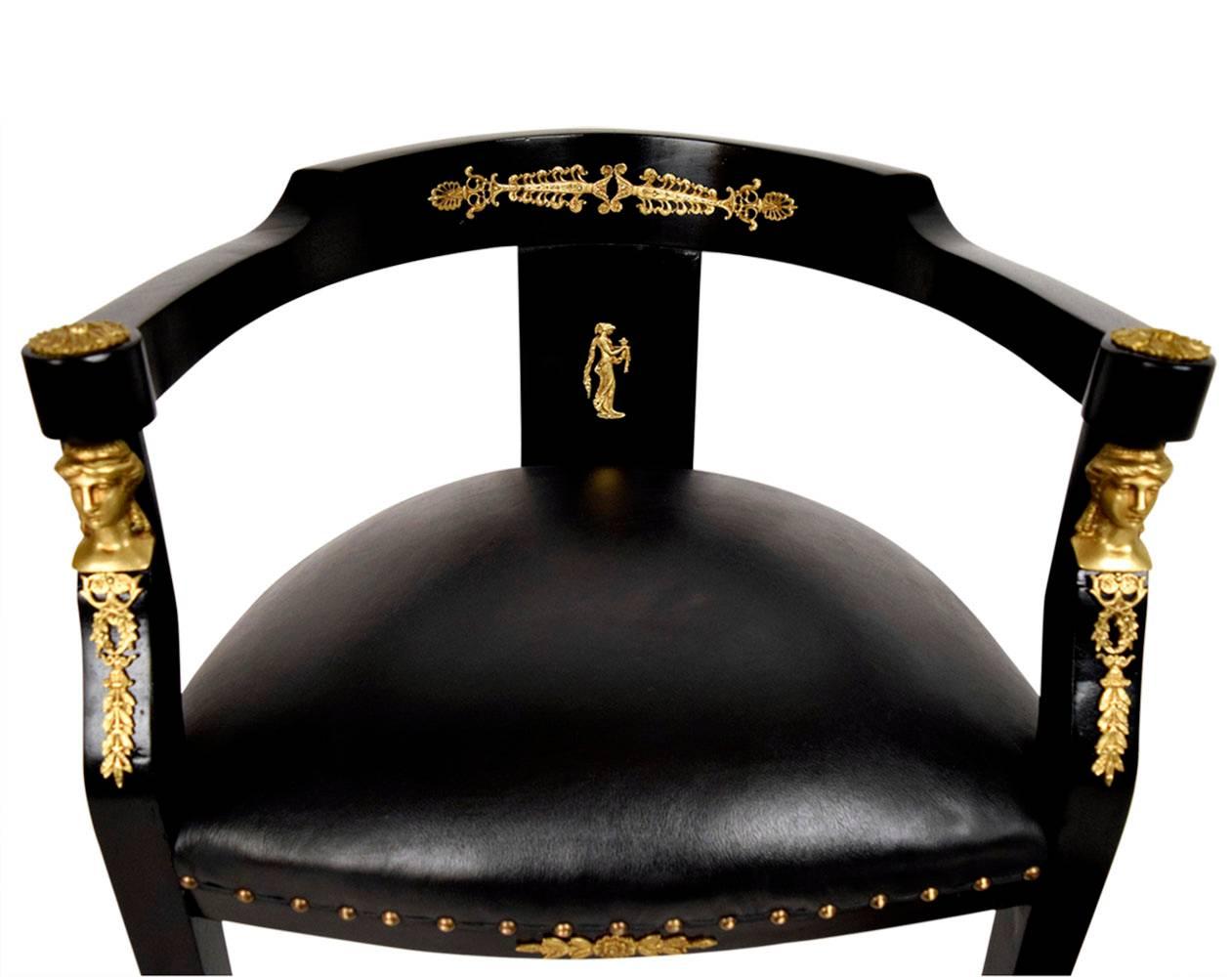 Elegant ebonized 1880s Empire style armchair. Solid wood, newly finished in a rich black color. Has a low curved back, that ends at the arms. Bronze ornaments complement the back, arms and bottom centre. Seat has been professionally upholstered in