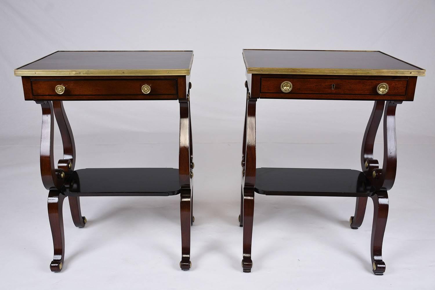 This 1910s antique English regency style pair of side tables is made from mahogany wood that has been finished in both a mahogany color and lacquered black stain. The wooden tops of the side tables feature brass moulding details. Below there is a