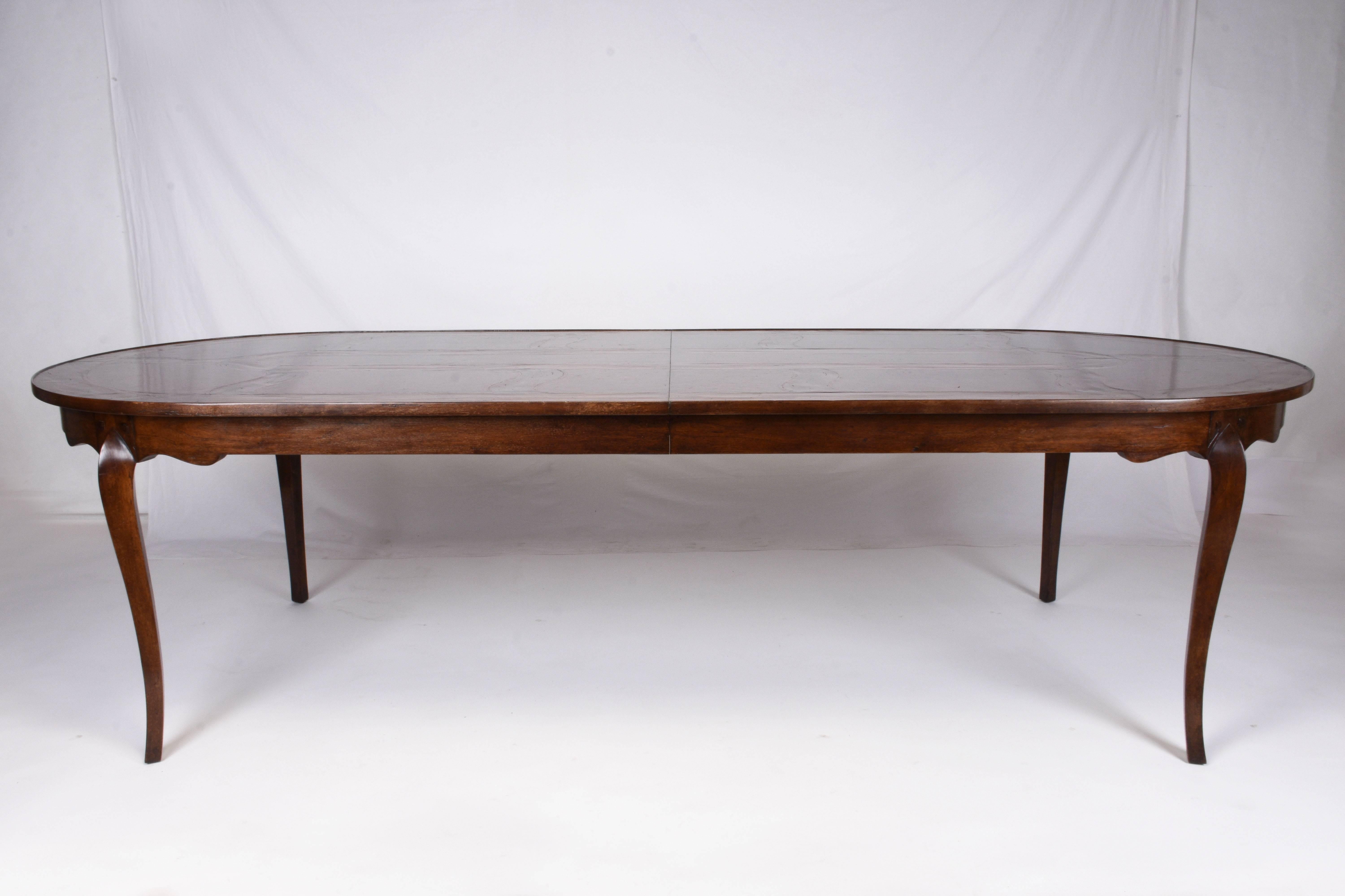 This 1950s grand Italian oval dining room table is made from walnut wood with beautiful inlaid details throughout. The dark walnut stained finish is off set by the honey colored inlaid patterns. The carved legs feature a serpentine shape that mimics