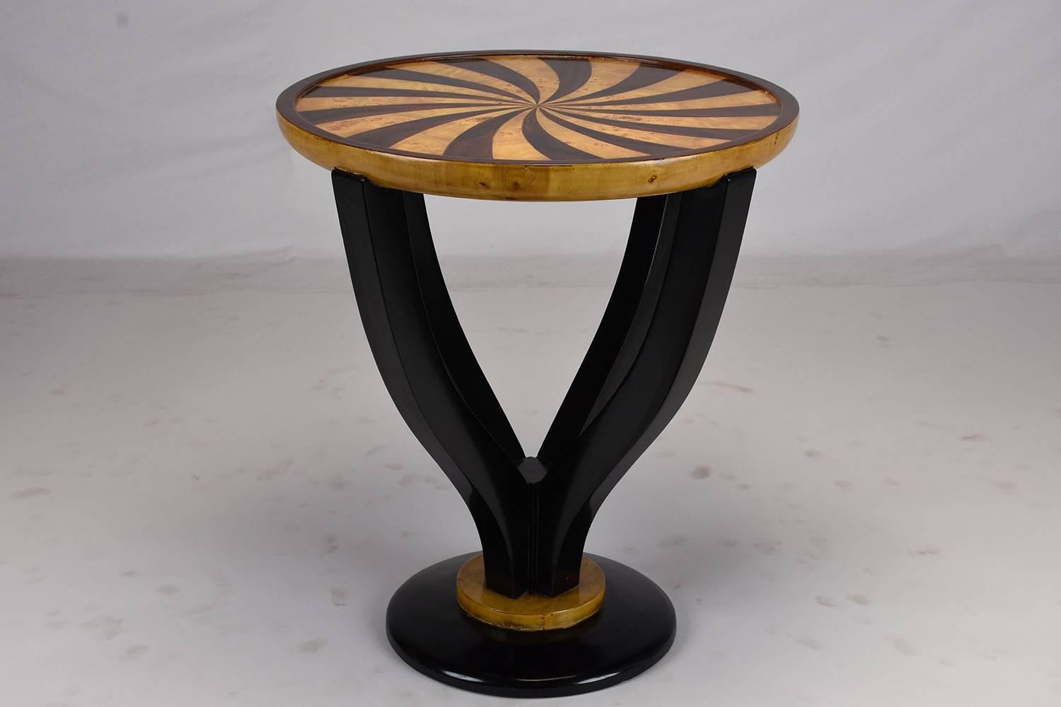 This 1980s vintage end table is made of mahogany wood and is adorned with burl wood veneers. The pedestal base of the table is stained in a rich black colored stain that is off set by the golden base and top. There are four arms to the base that