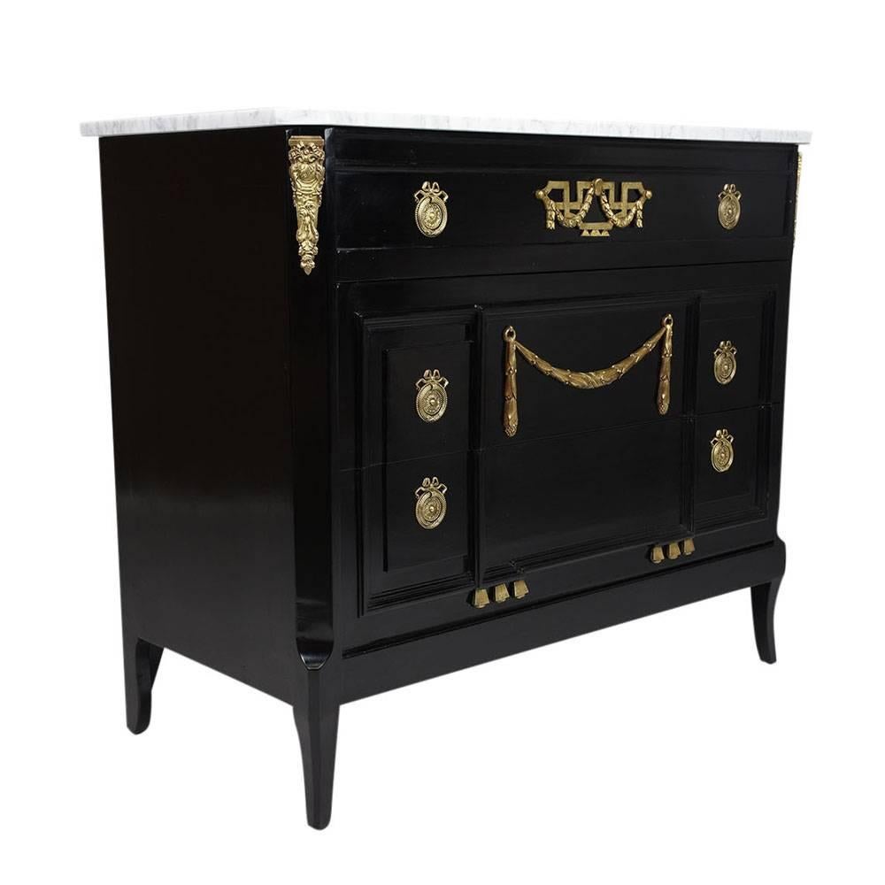 This 1930s pair of French Louis XVI-style commodes are made of mahogany wood that features a beautiful ebonized finish. This two-drawer commode is uniquely adorned with moulding details on the facade and is accented with brass ormolu of garlands and
