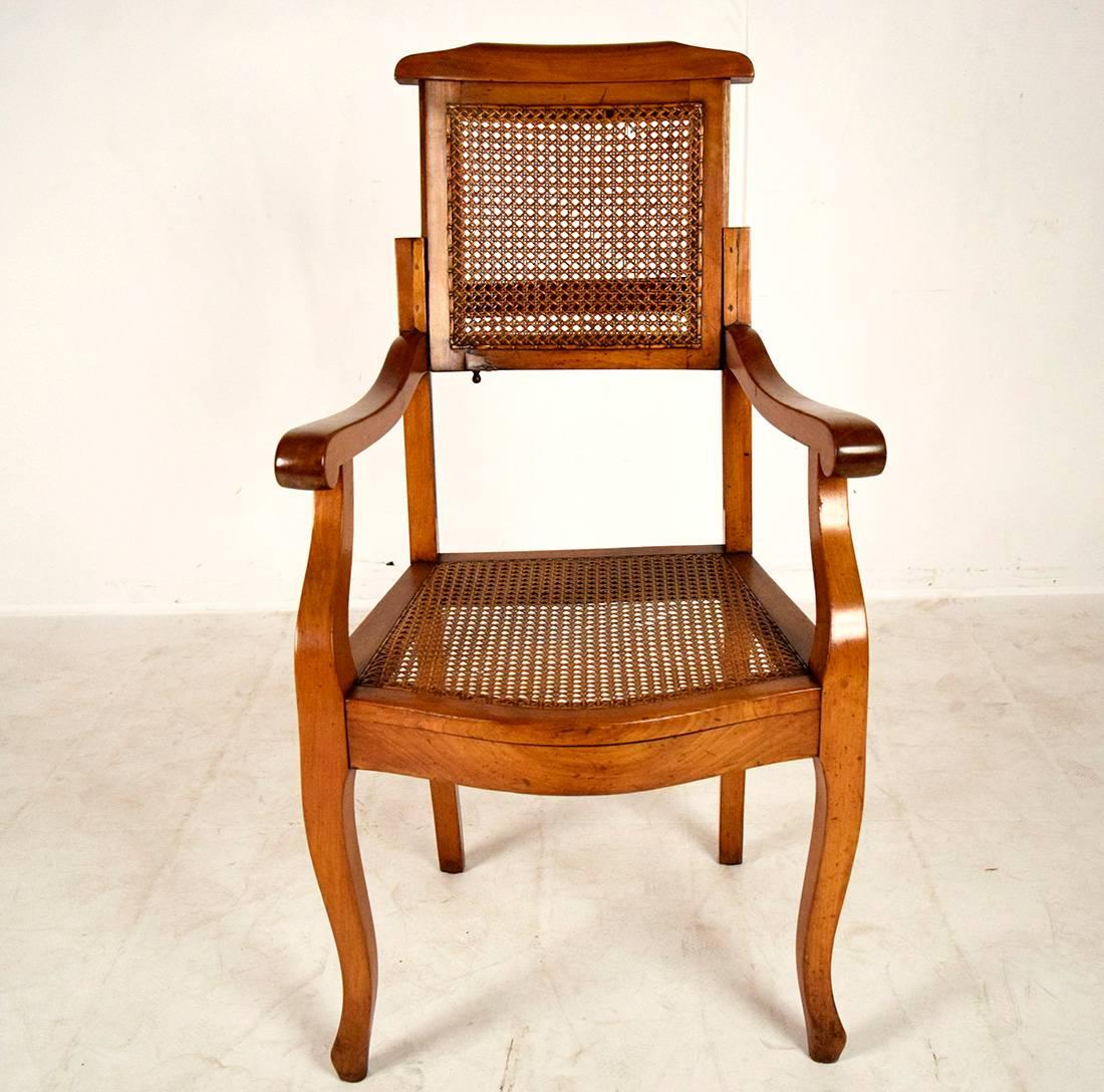 This unique 1840s French Empire style Directoire office chair features a solid walnut wood frame with its original walnut color finish. The seat and back have caning finished in original walnut color. The chair frame shows the original patina. This