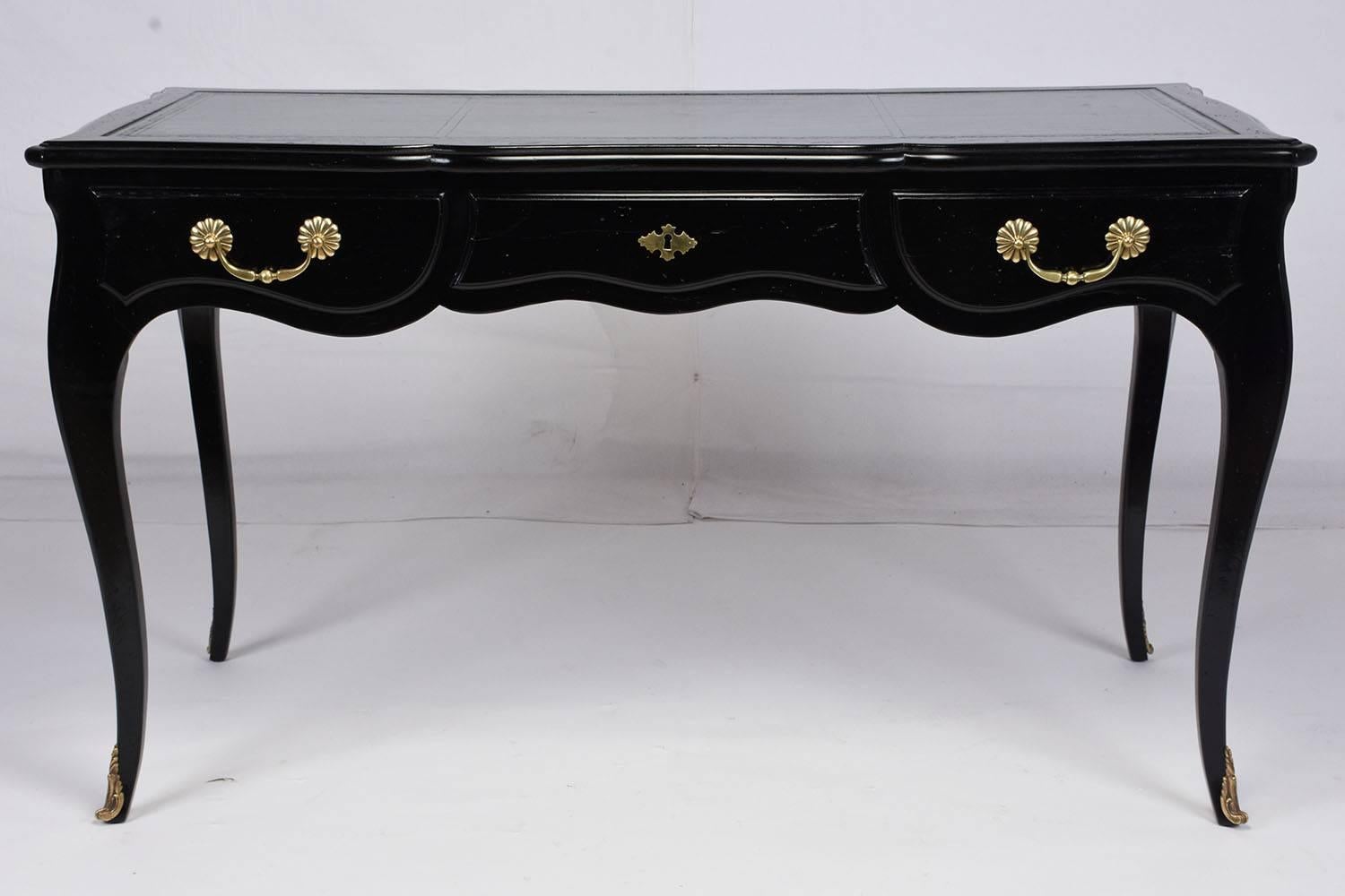 This 1970s Louis XV-style desk is made by Auffray & Co. and features carved wood in a beautiful ebonized finish. The carved facade features a scalloped bottom with graceful serpentine legs. The three drawers feature decorative brass drawer pulls and