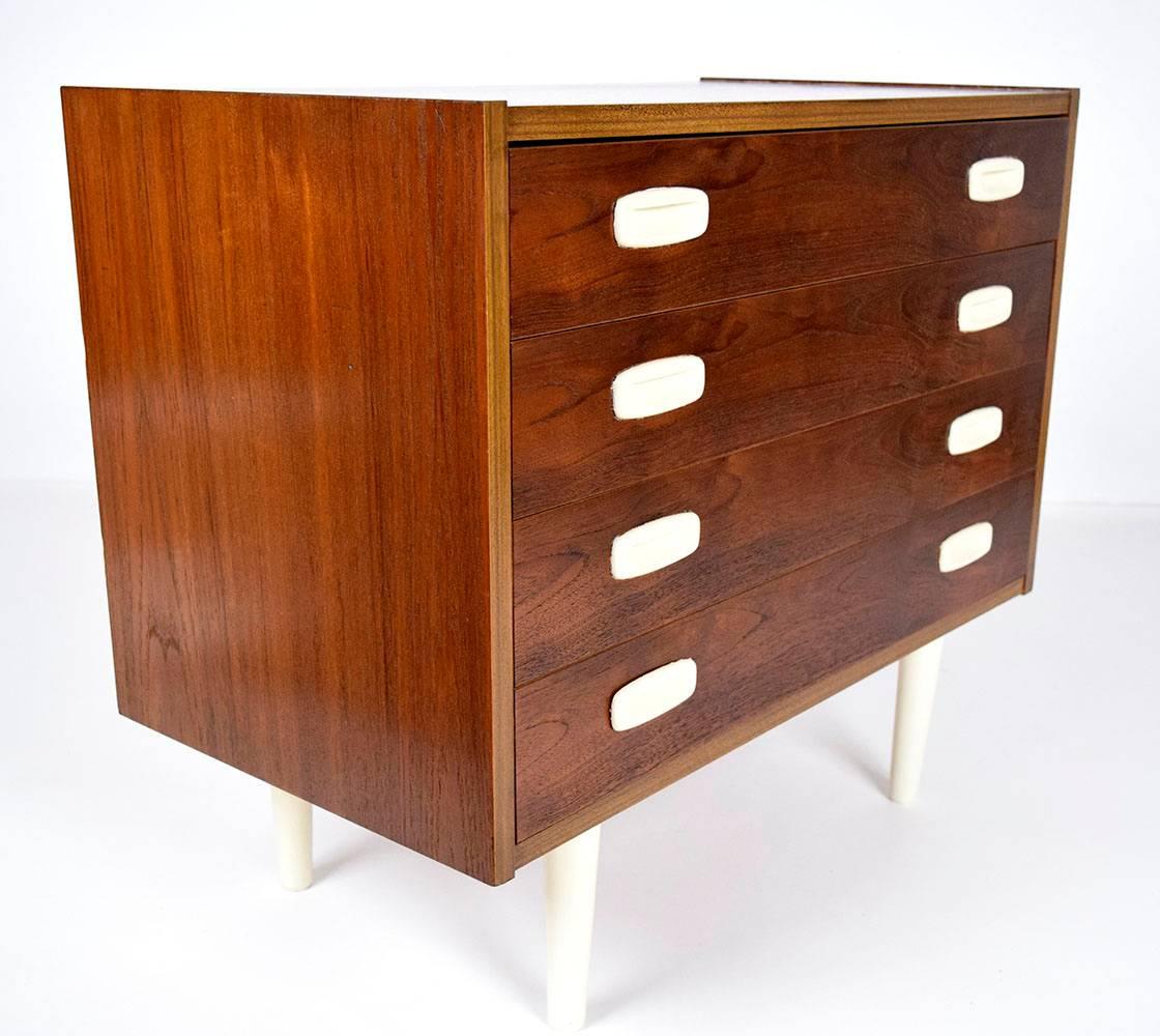 This 1960s Danish modern occasional chest is made of walnut wood with a walnut stain finish. There are four full size drawers with dovetail joints. The simple and clean lines of this chest are accented by the off-white drawer pulls and tapered legs.