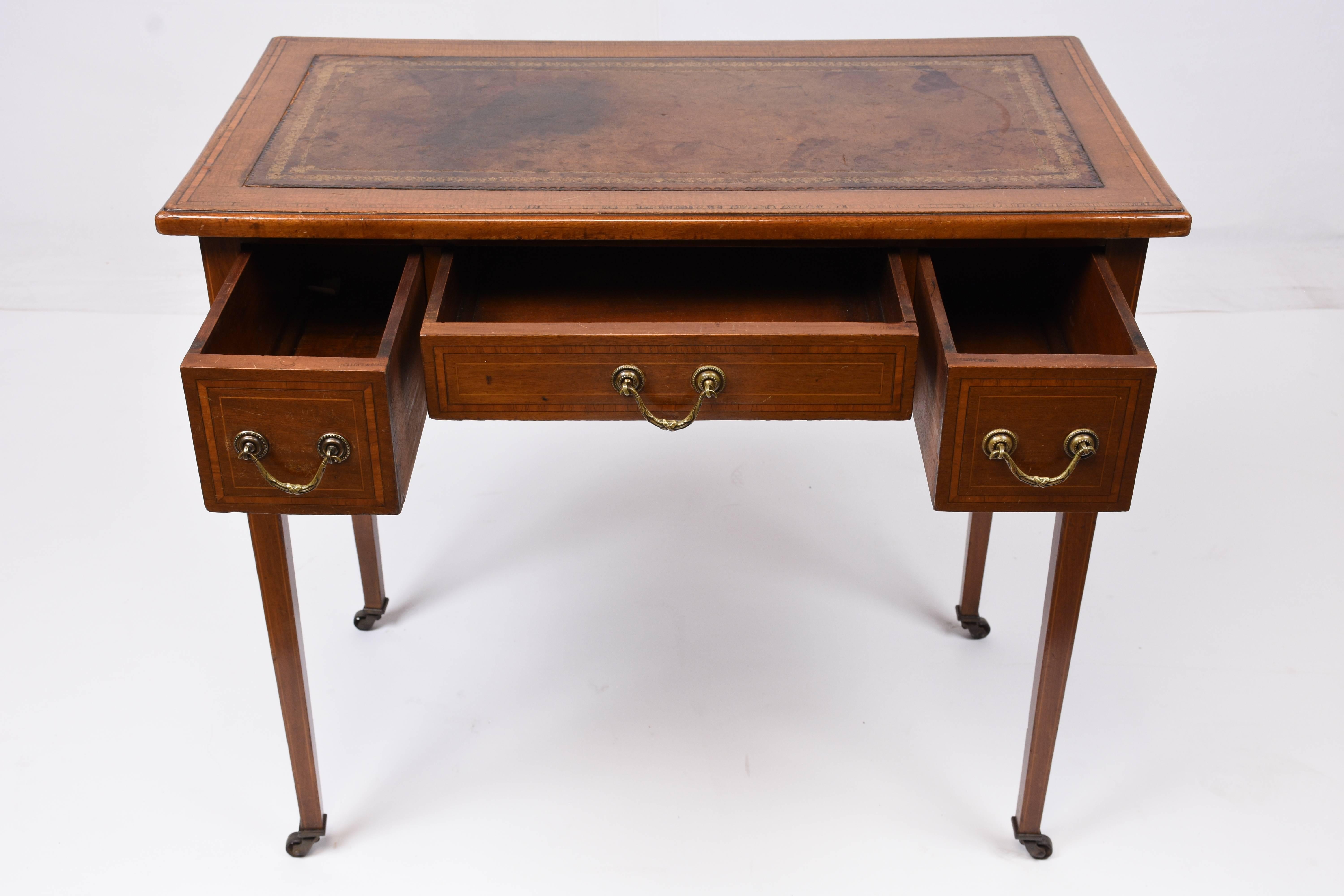 This 1870s antique English traditional-style writing desk is made from mahogany wood in its original mahogany color stain. The top of the desk is adorned with the original embossed leather work area with gilt trim details and an inlaid wood boarder.