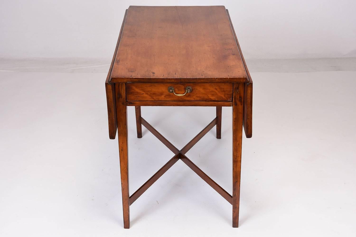This 1880s English Sheraton Pembroke-style side table is made of mahogany wood with its beautiful original mid wood tone finish. There are two leafs that extend on either side of the side table for extra space. The stretched legs form an X-shape