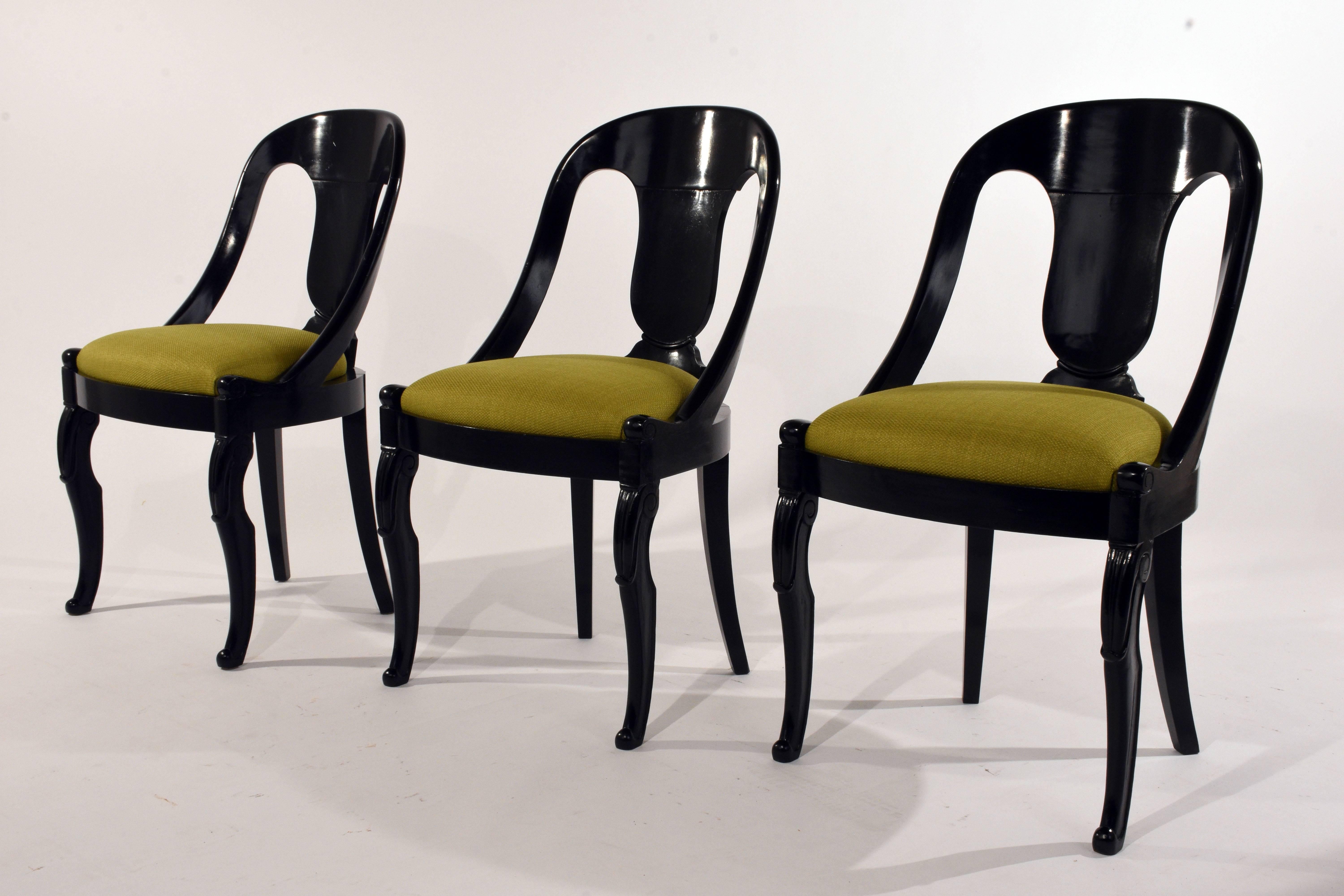 This set of six 1930s Empire-style dining chairs feature mahogany wood frames that have been ebonized with a lacquered finish. The curved gondola back shapes the back of the chairs and leads into the carved serpentine legs. The carved legs haves