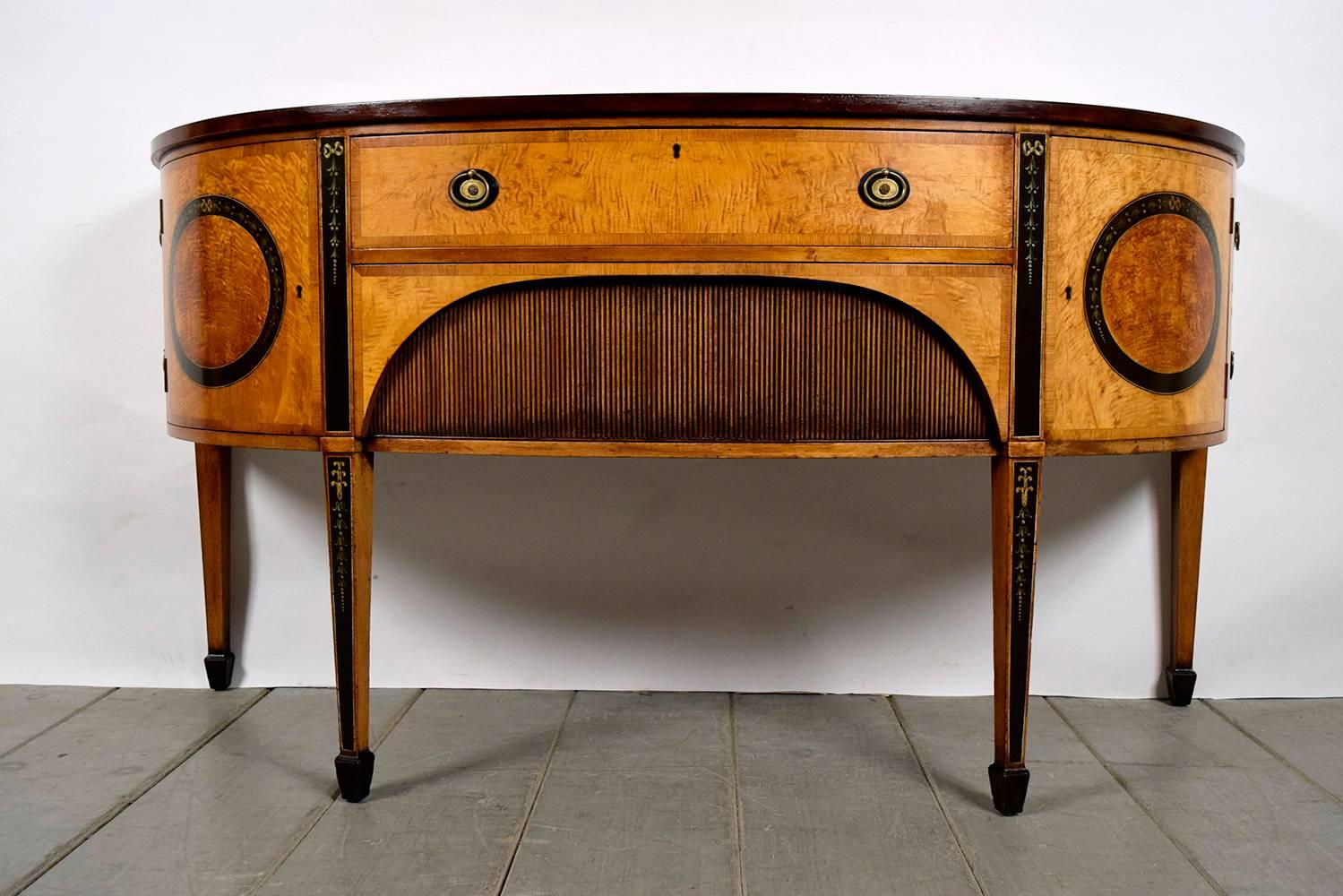 This is an Edwardian-style sideboard made with of solid wood with a stunning and inlaid decorated top. The demilune shape design with burl veneers on the front and sides is unique. The sideboard features two front drawers and two curved side doors.