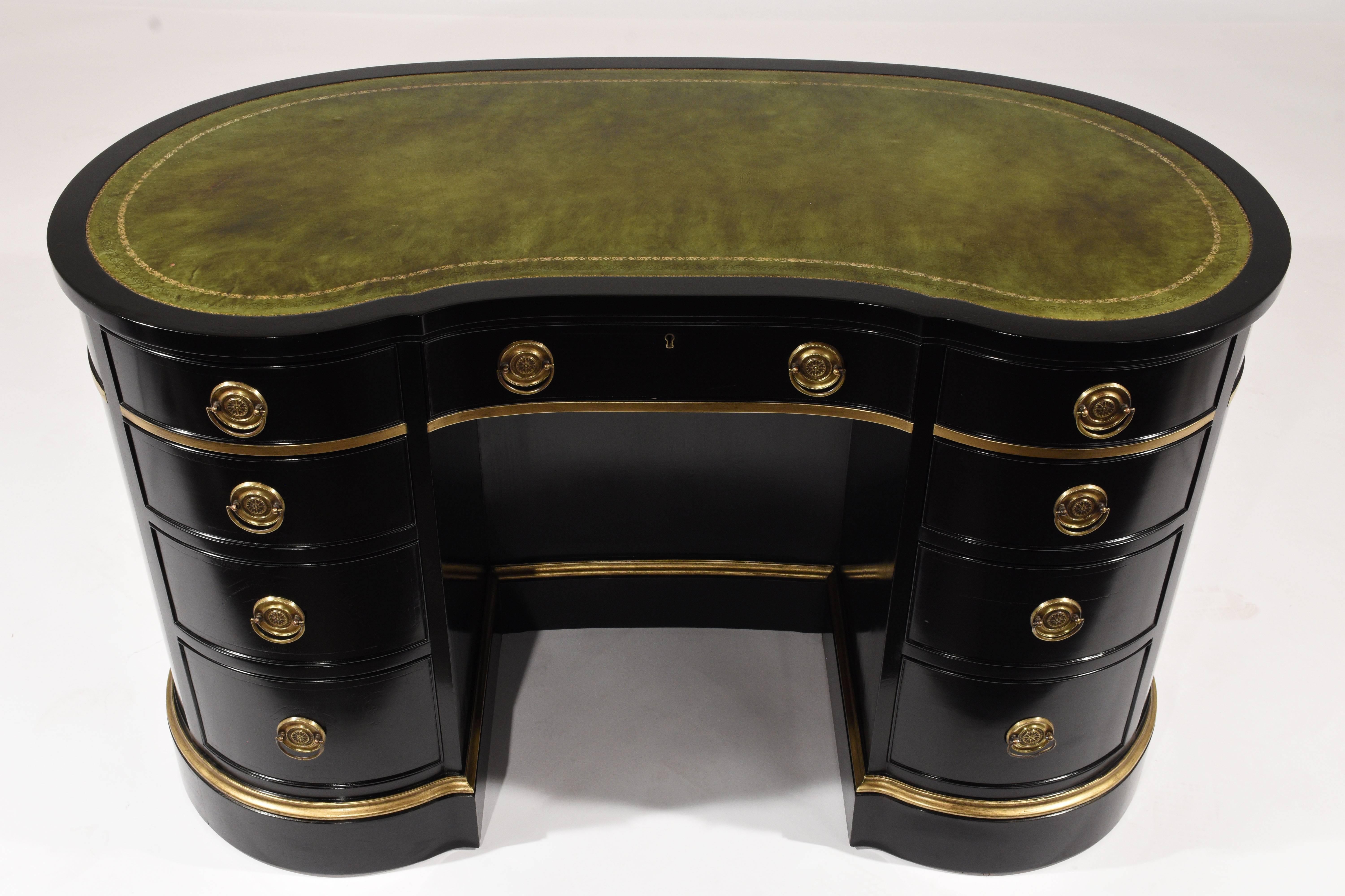 This 1950s vintage Regency-style kidney shaped desk is made of wood that has been ebonized with a lacquered finish. Adorning the pedestal legs are carved mouldings with gilt details. There are four drawers with decorative brass drawers pulls in each