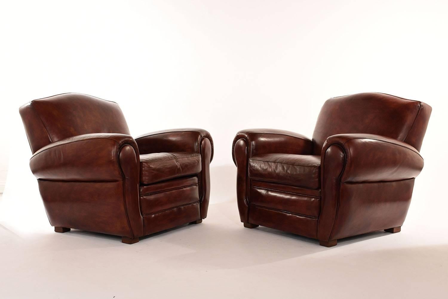 This pair of Art Deco-style club chairs is fully upholstered in leather. The rounded back and arms are accented with nailhead trim on the backside. The comfortable seats feature a single loose cushion and accented with single piping trims. The