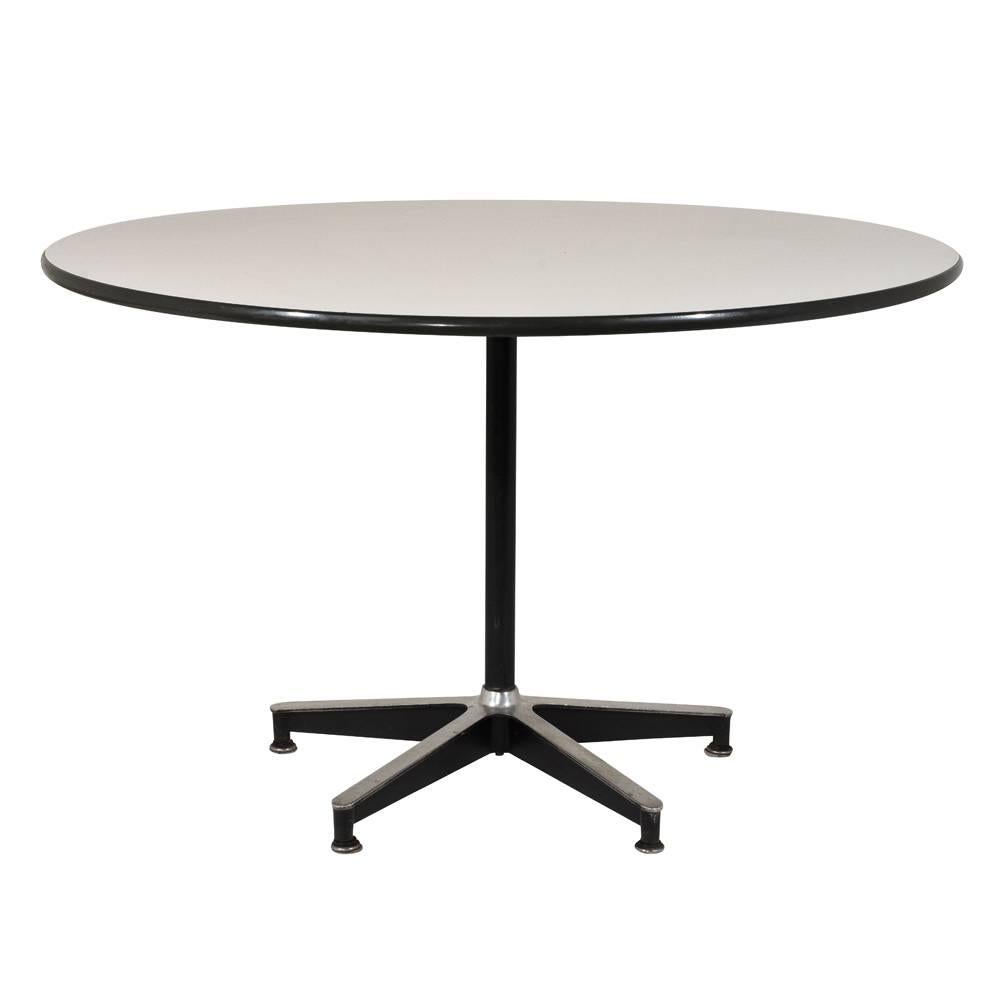 This 1960s Mid-Century Modern Dining Table is designed in the manner of Herman Miller and features a white formica surface with black trim. The center table has a circular top that rests on pedestal legs made out of steel with black accents and