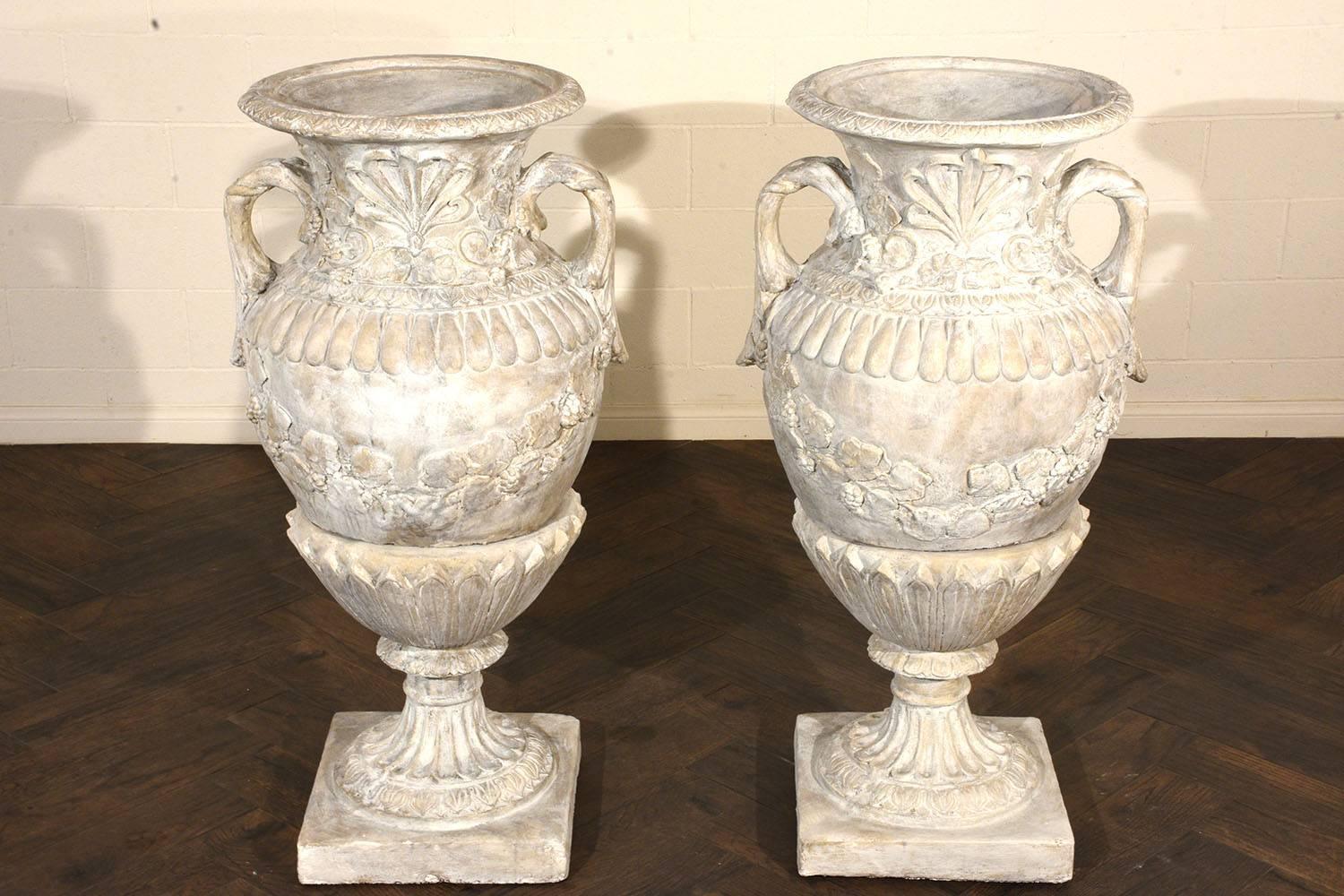 This pair of 1980s vintage grand patio urns are made of cast stone that have been painted in an off-white and grey combination using a white washing technique. The urns are adorned with ornate details of ripe vineyard vines, acanthus leaves, and