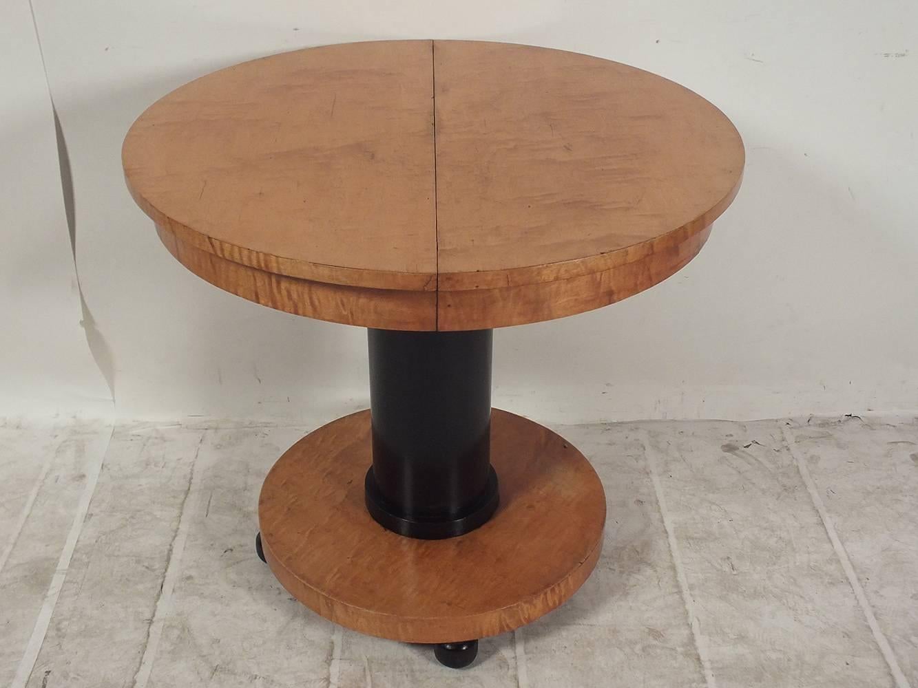 This late 19th century Biedermeier-style center table is made of solid wood with its original, rich golden color stain. The simplistic style of the table is accentuated by the single circular pedestal leg that has been finished in a rich black