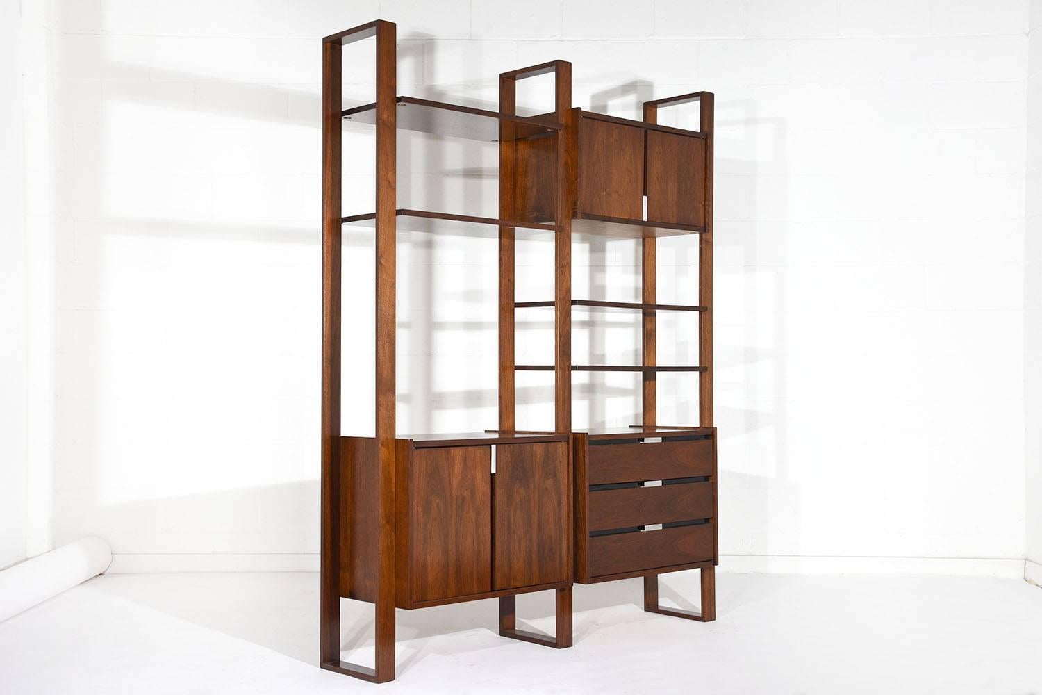 This 1960s Mid-Century Modern style freestanding wall unit bookcase is made from walnut wood stained in a rich, dark walnut color with a lacquered finish. There are two cabinet sections with ample storage space and are opened by the aluminium pulls.