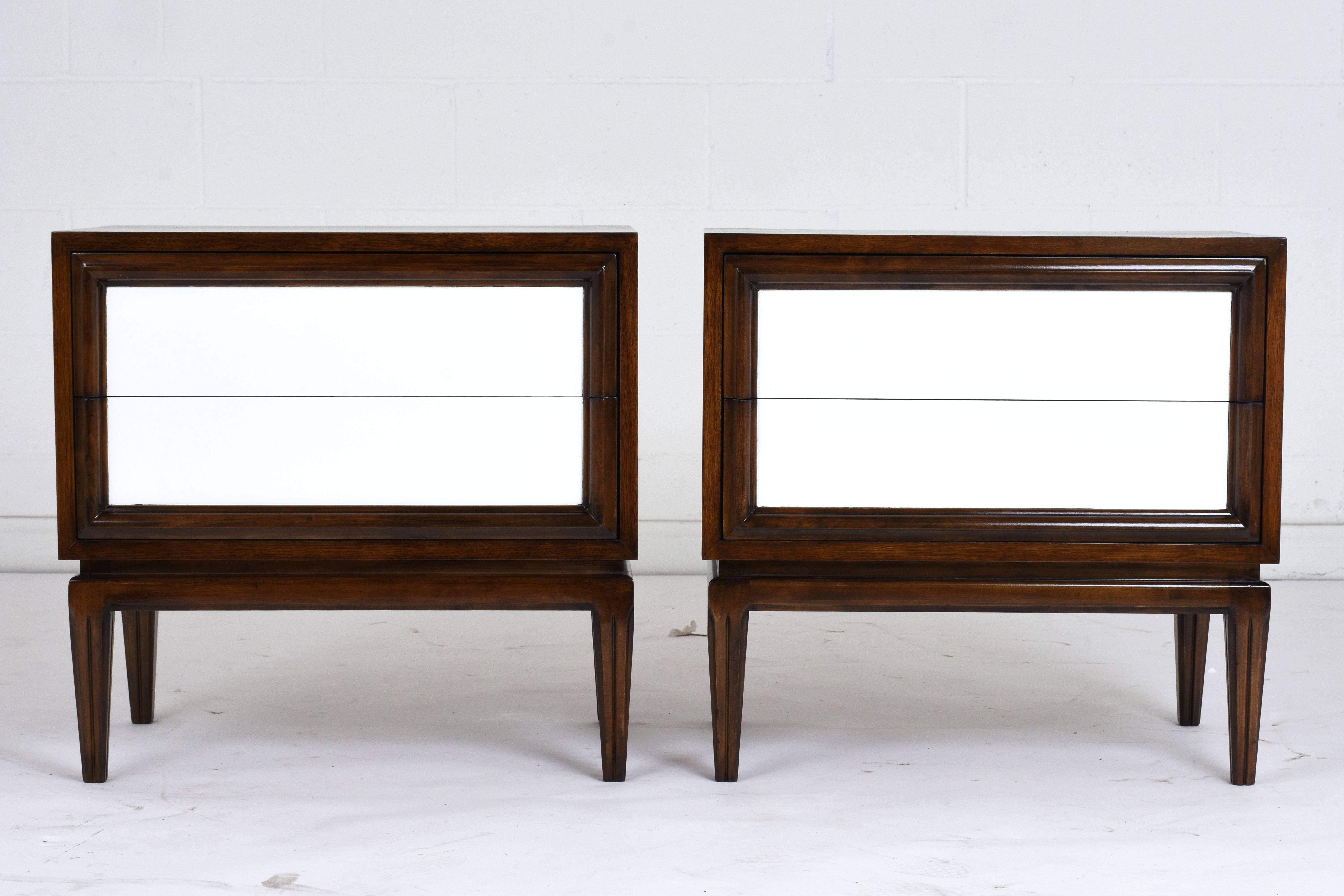 This pair of 1960s Mid-Century Modern-style nightstands are made of walnut wood finished in two tones. The wood frame is finished in a rich walnut color and a sleek profile. The two drawers feature carved moulding along the edges and a bright white