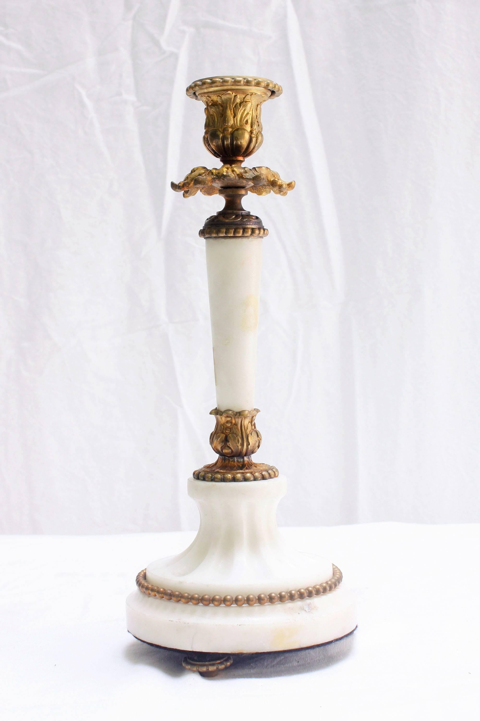 This pair of 1880s, French Louis XVI-style candlesticks are made of marble and bronze. The shaft and base of the candlesticks feature carved white marble that is unpolished. The base is circular and has fluted details. The bronze accents are