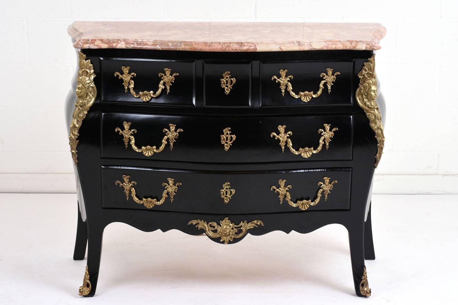 This 1930s, French, Louis XVI-style commode is made of wood ebonized in a rich black color with a lacquered finish. The curved sides of the chest is accented by ornate brass decor. The ormolu on the edges feature a woman's face surrounded by