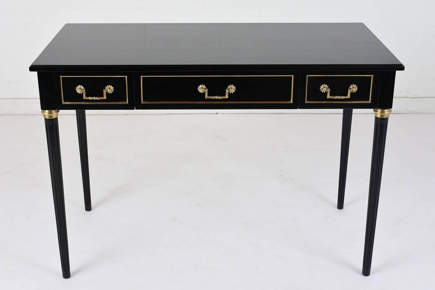 This 1900s French Louis XVI-style desk is made of mahogany wood ebonized in a deep black color with a lacquered finish. The desk features three drawers with brass moulding accents an decorative brass handles with rosettes details. The carved legs