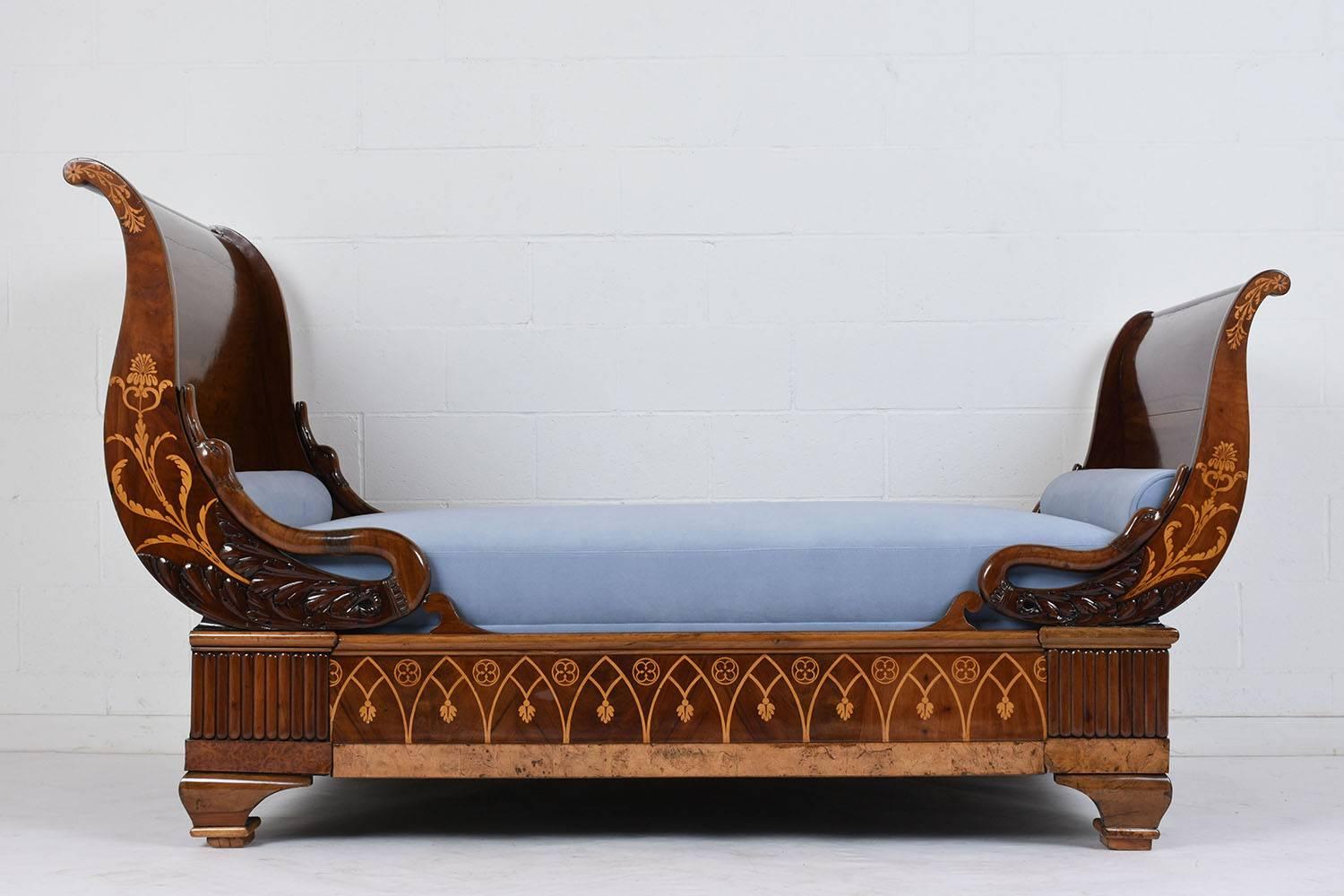 This 1850s French Empire-style daybed features a wood frame stained in a fruitwood color with a lacquered finish. The sleigh-style frame features intricate inlaid details on the headboard and footboard of flowers, leaves and Gothic motifs. The