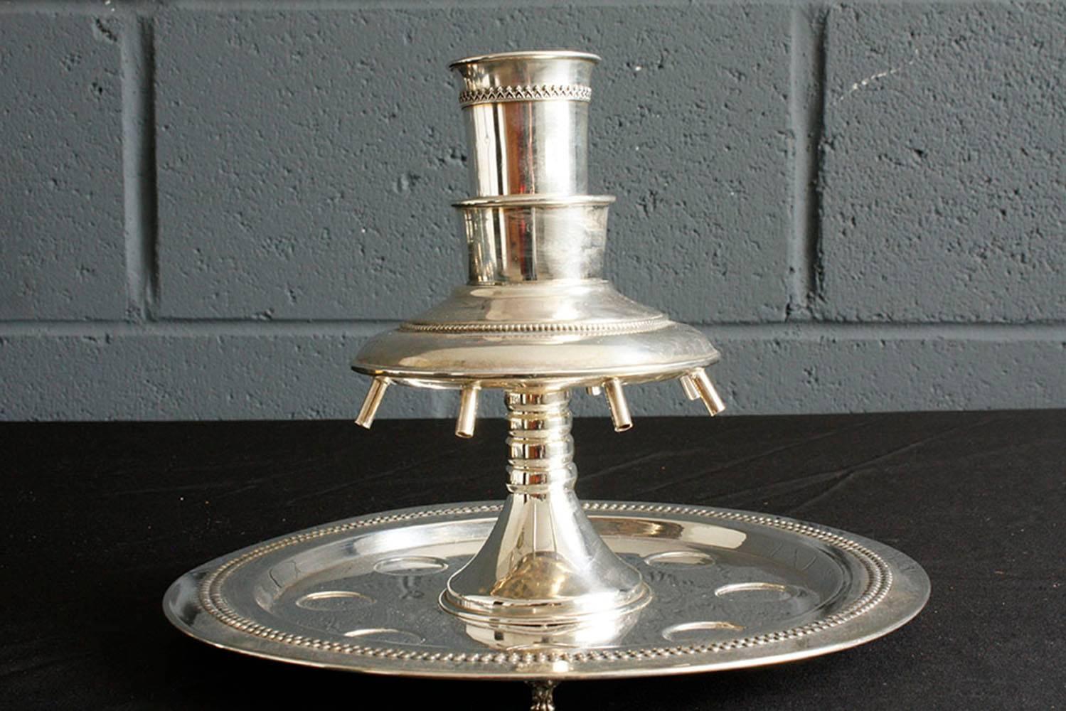 This 1950s Judaica-style wine fountain is made of sterling silver. The set includes the wine fountain base, a larger waterfall cup, and eight drinking cups. The set is stamped .925 sterling silver. The wine fountain would made a great hosting piece