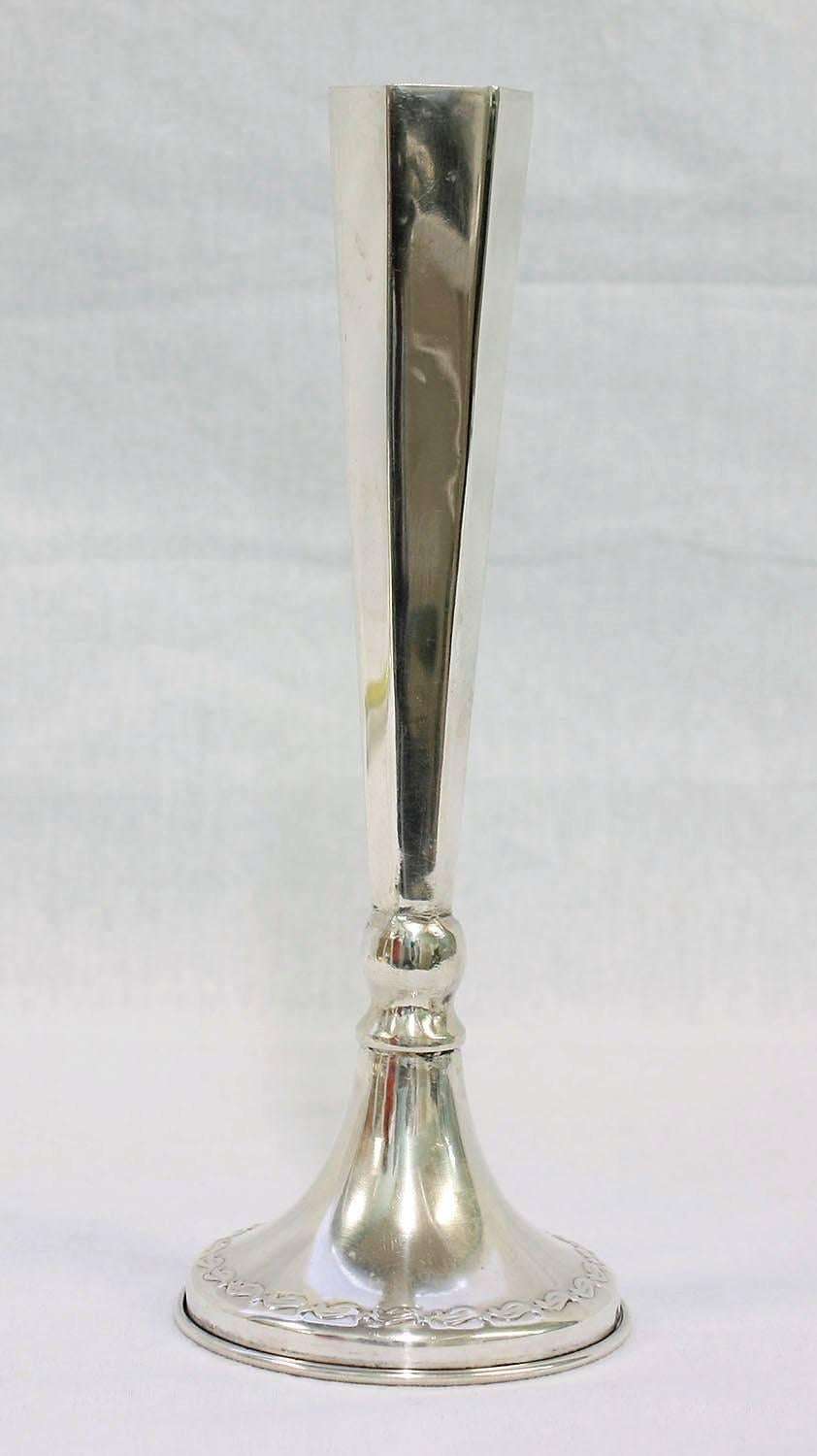This pair of Art Deco-style candleholders is made of sterling silver and stamped .800. The candle holders have a unique shape that resembles a champagne flute and is accented with faceted details and a leafy trim around the base. This pair of candle