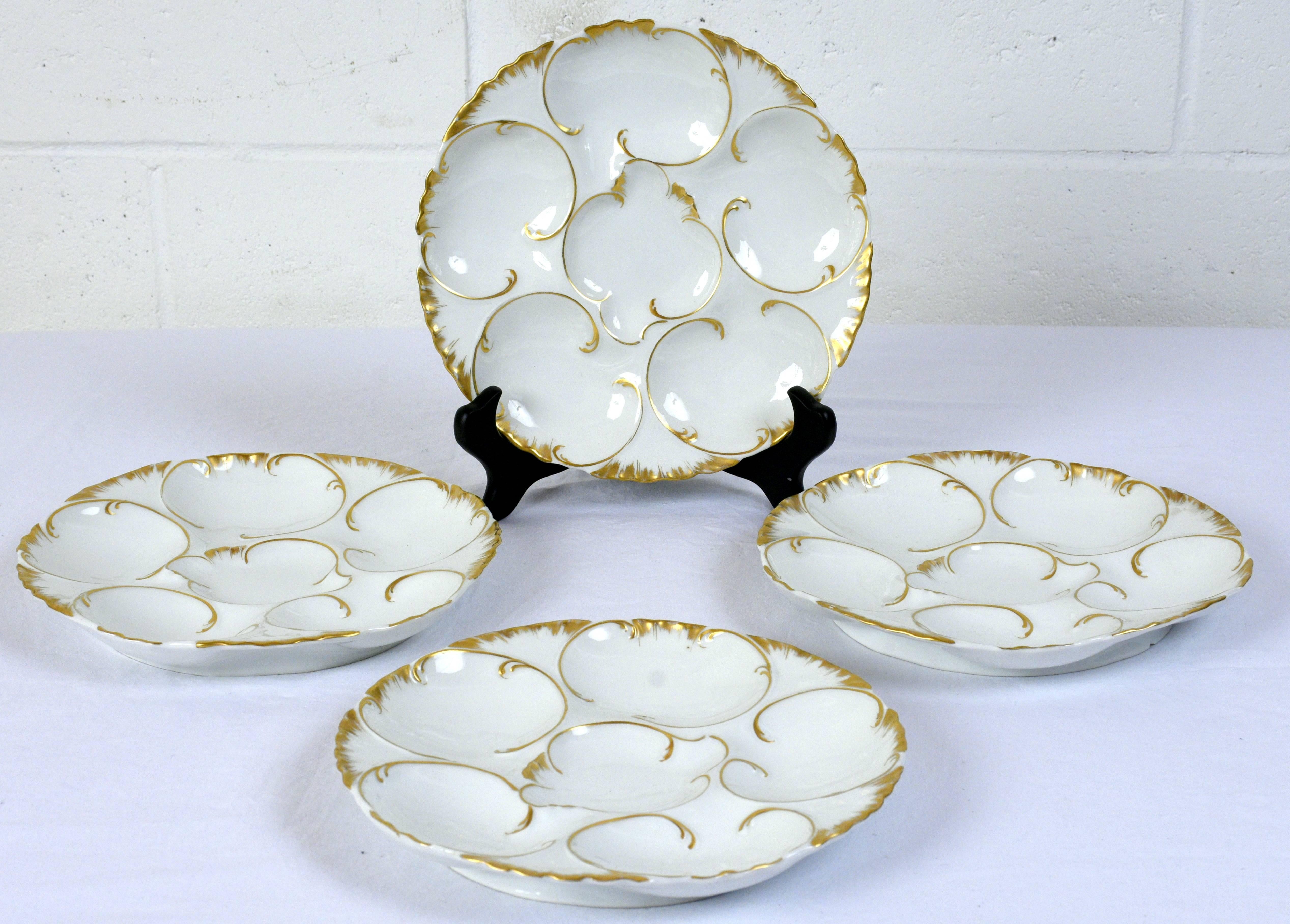 This set of eight 1970s oyster plates are made of porcelain with gilt trims. The round plates have a scallop design edge and feature six places for oysters in the centre of the plate. The plates are accented by leaf details. The plates are marked