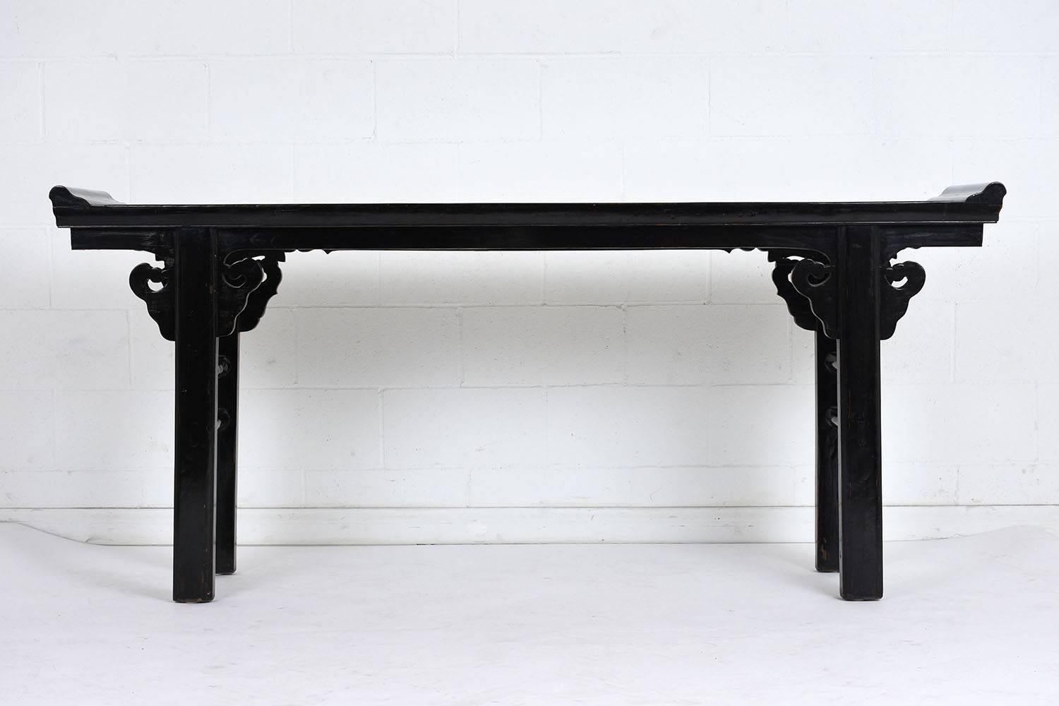 This 1960s Chinese altar table is made of wood with an ebonized and lacquered finish. The table is adorned with carved leafy accents and has scroll accents at the ends of the table. The legs feature a ladder stretch bar. This altar table is sturdy,