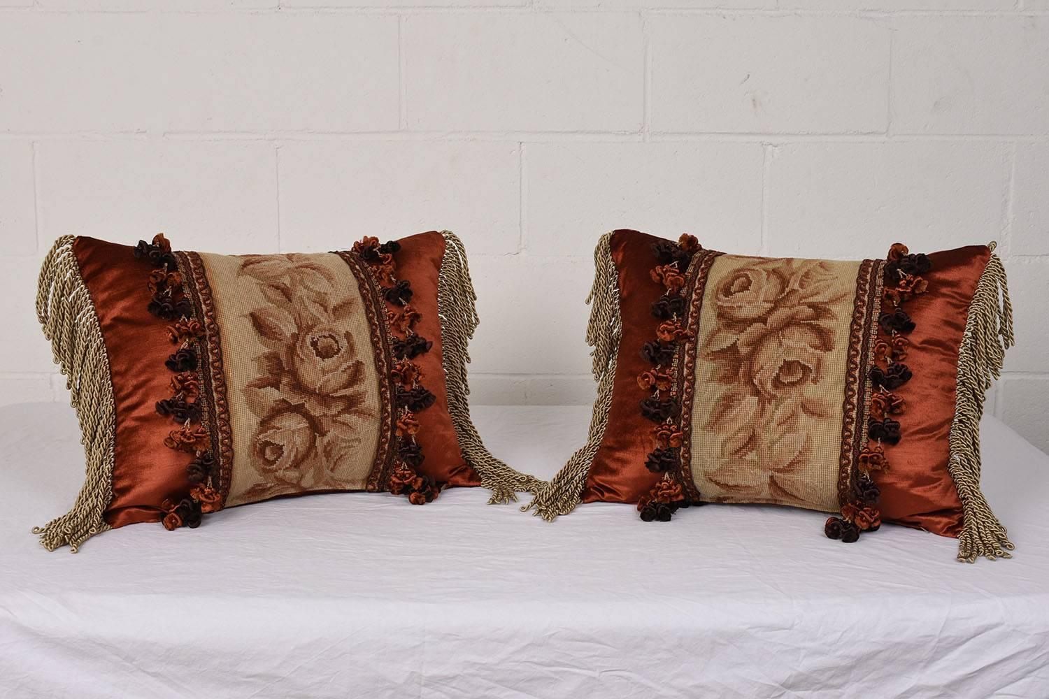 This set of three throw pillows feature antique Aubusson tapestry panels. The tapestries depict roses, leaves, and vines with simple decorative details. The border of the panels is accented by ornate multicolored tassels. The pillows are finished