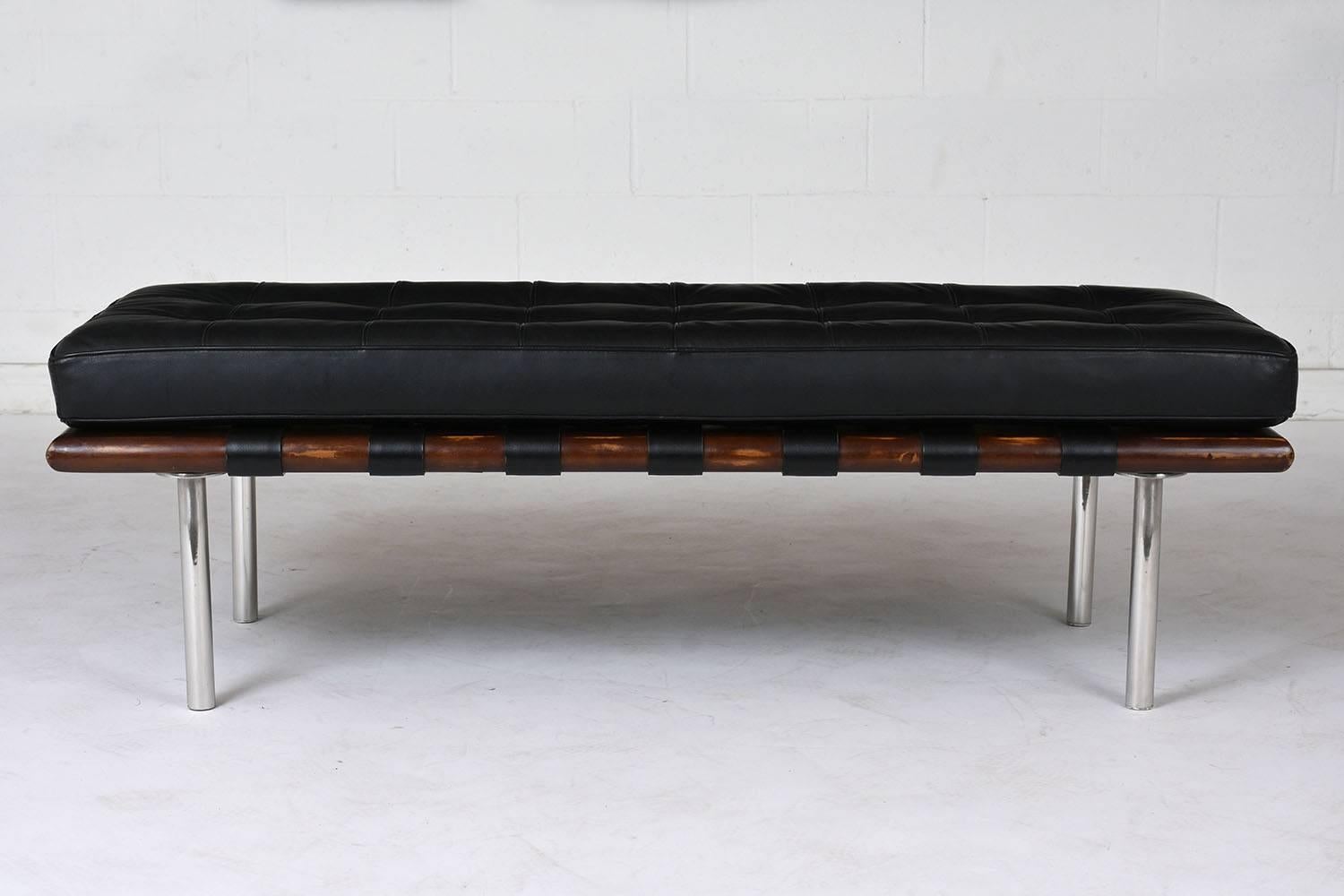 This 2000s Mid-Century Modern-style bench is made in the manner of Herman Miller. The bench features a wood frame stained in a walnut color with chrome legs. The bench supports its cushion with leather straps wrapped around the width of the bench.